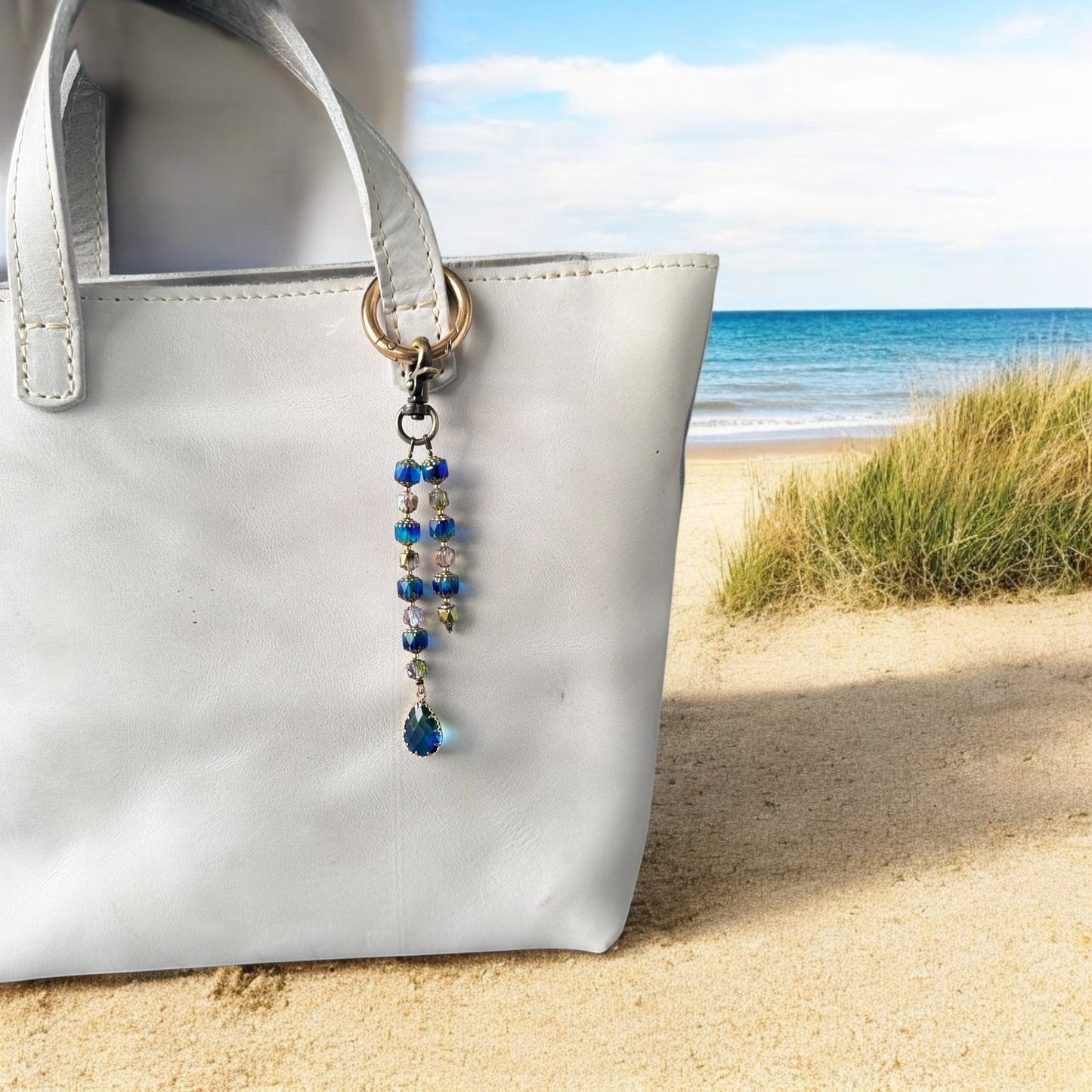 A white designer handbag with a crystal beaded keychain and a teardrop pendant, displayed against a festive background with Christmas decorations.