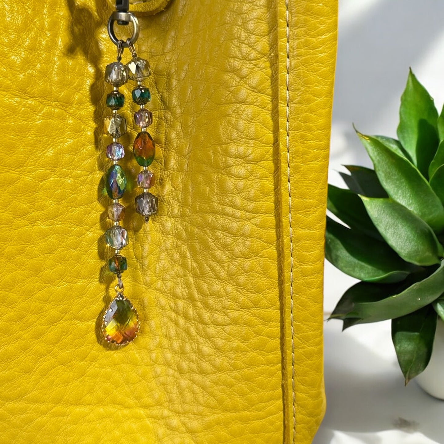A yellow designer handbag with a crystal beaded keychain and a teardrop pendant, displayed against a festive background with Christmas decorations.