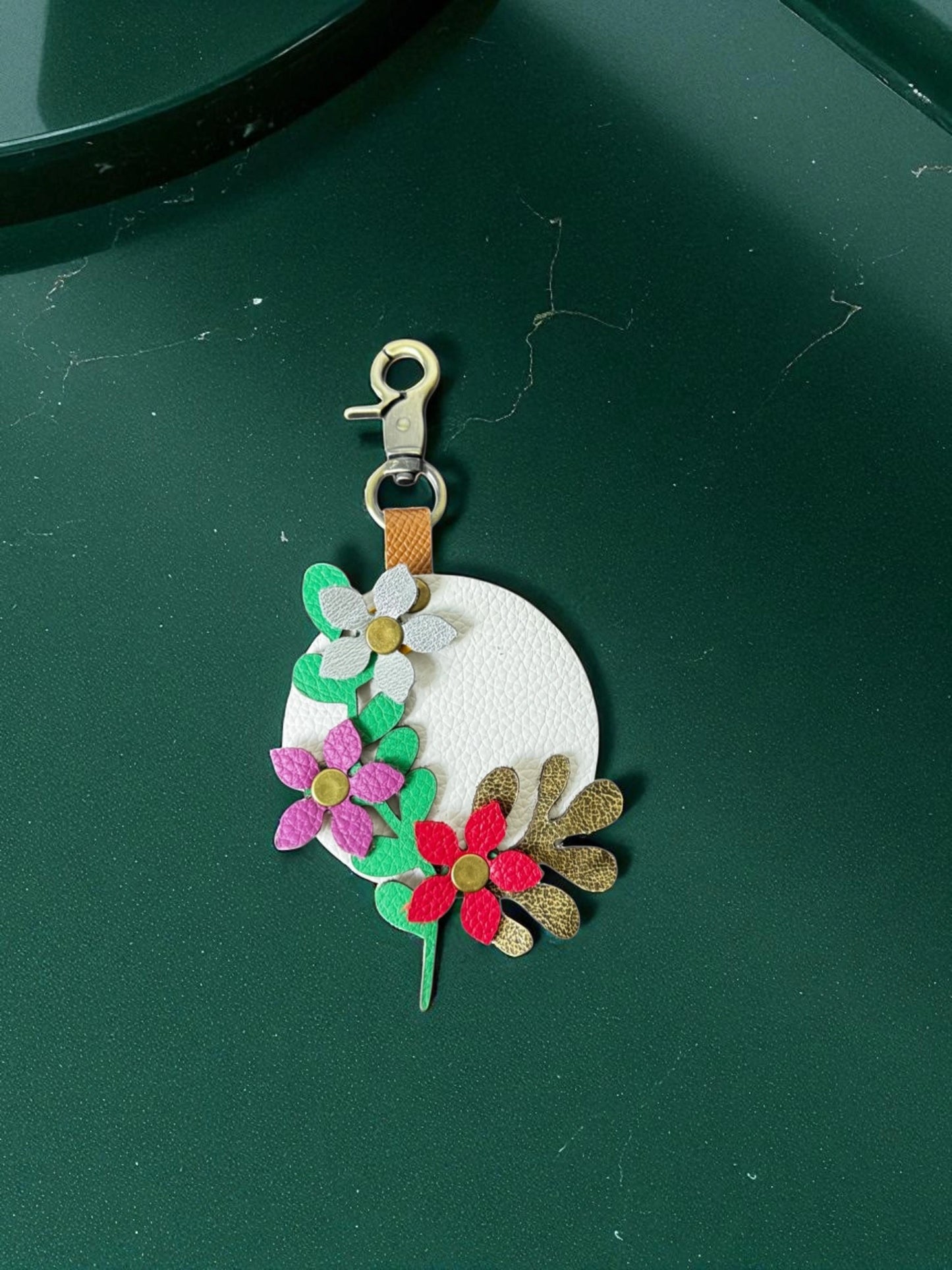 Floral keychain with a white circular center on a green surface