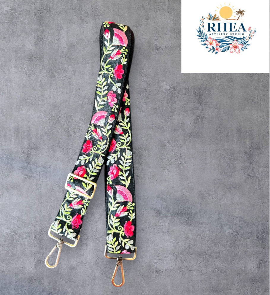 An adjustable embroidered purse strap with a floral pattern and gold hardware, displayed against a grey background.