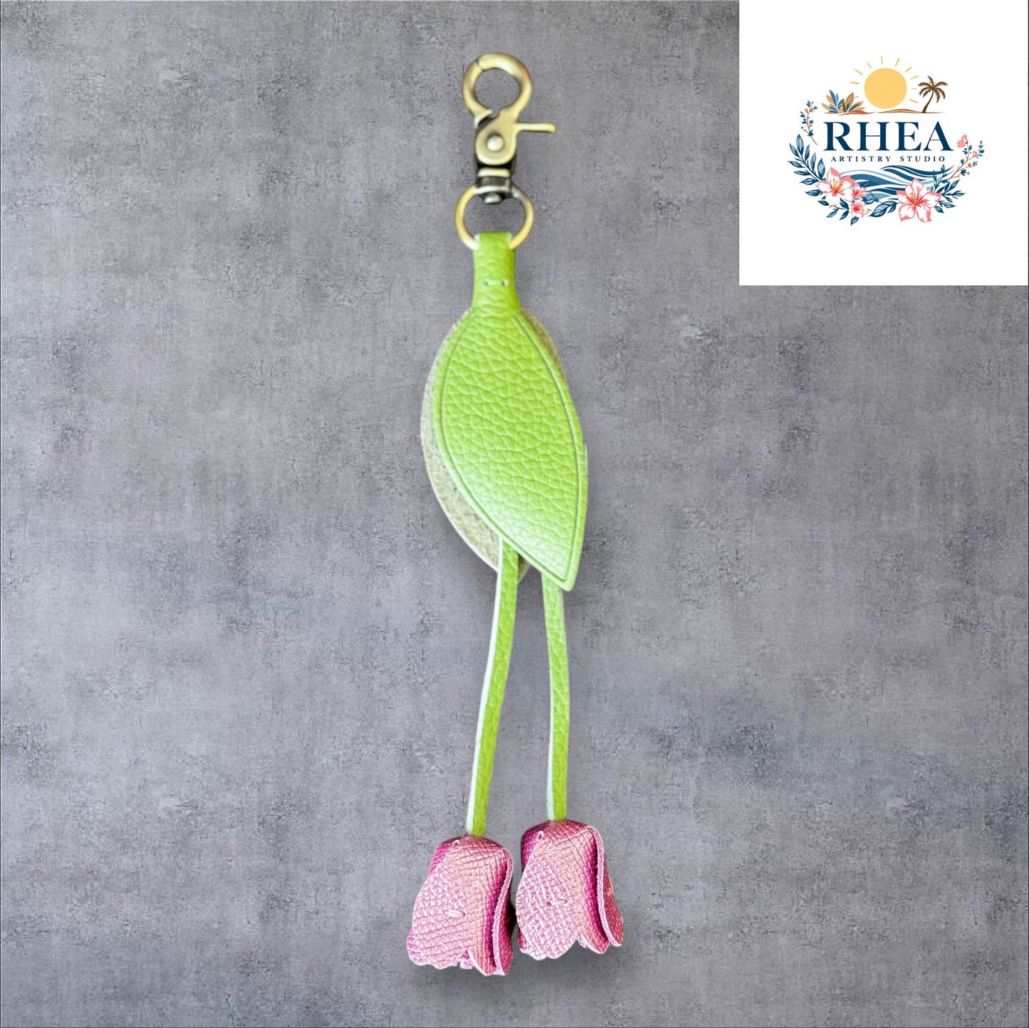 A handmade leather tulip charm with a green leaf and brown floral pattern, attached to a gold lobster clasp on a white marble surface.