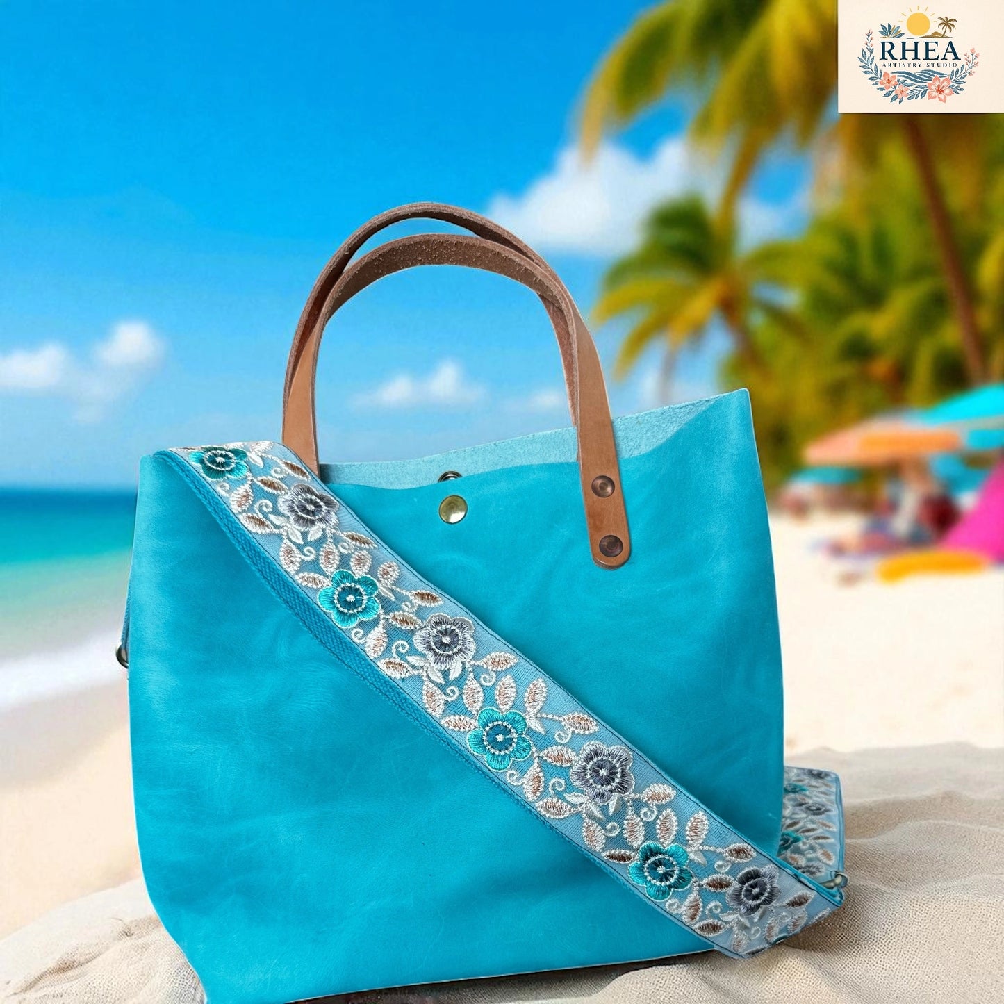 Blue handbag with floral embroidery on a beach with palm trees and ocean in the background.