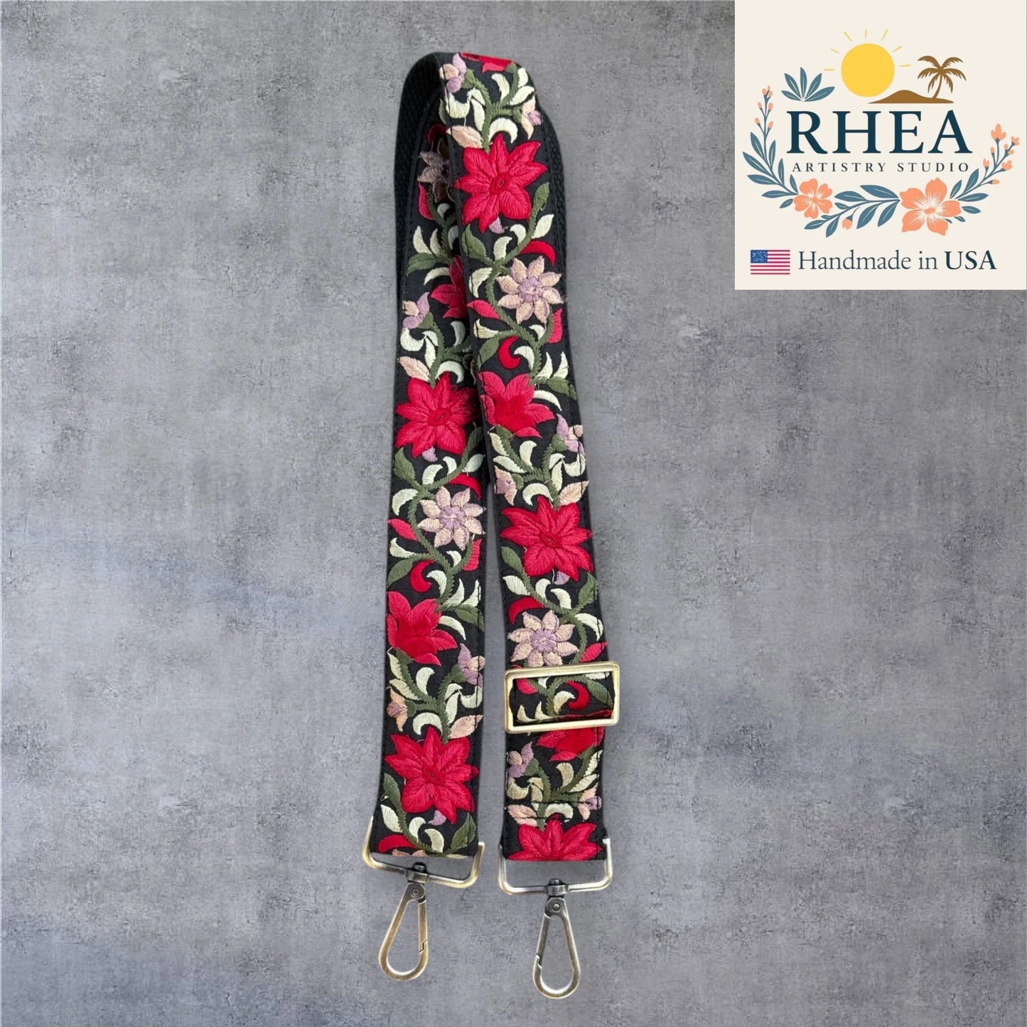 Floral embroidered purse strap with gold hardware on a gray background, featuring RHEA Artistry Studio logo.