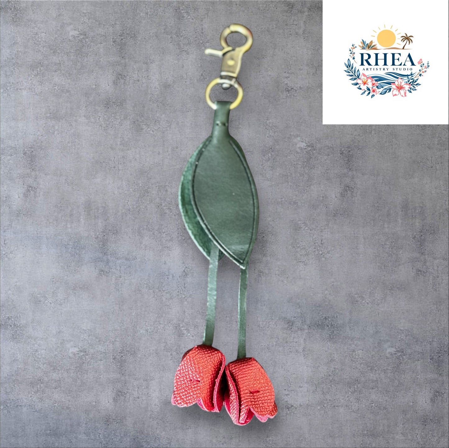 A handmade leather tulip charm with a green leaf and brown floral pattern, attached to a gold lobster clasp on a white marble surface.