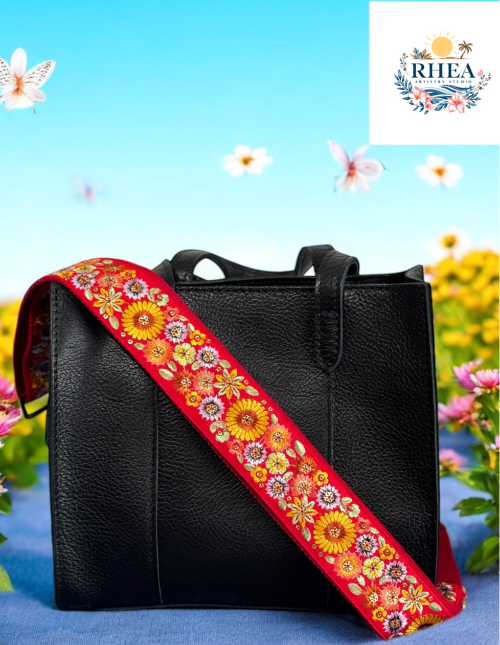 A floral embroidered purse strap in multicolor, attached to a black leather bag with brushed brass hardware.