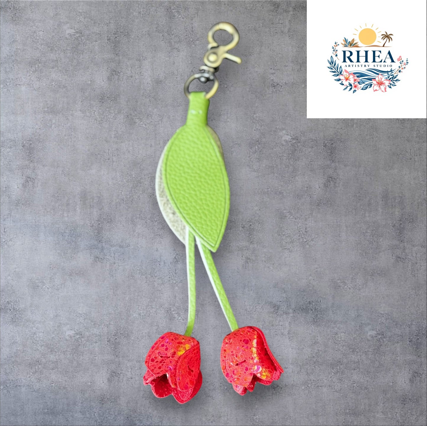 A handmade leather tulip charm with a green leaf and brown floral pattern, attached to a gold lobster clasp on a white marble surface.