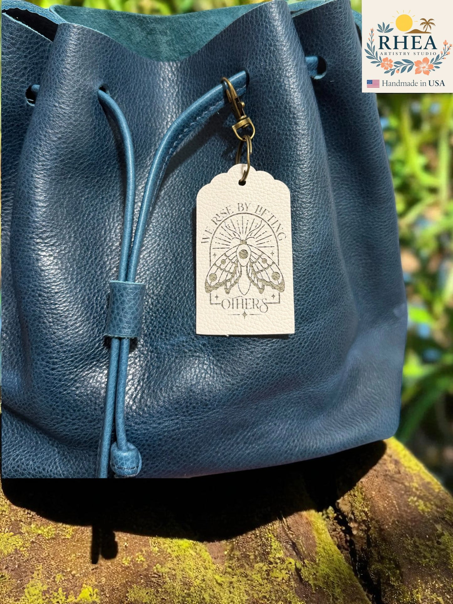 Blue leather bag with a tag on a natural background, featuring the RHEEA brand.