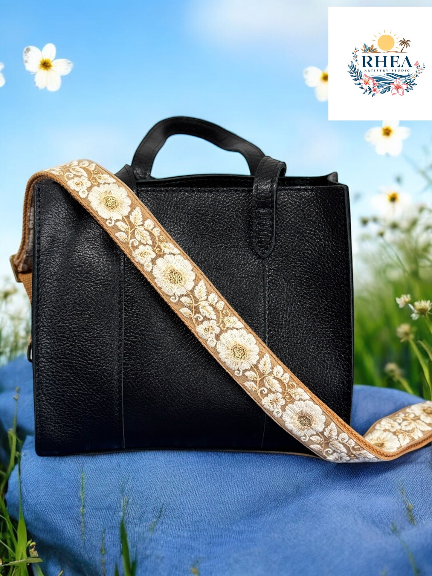 A black purse with a beige and green floral embroidered strap placed on a blue surface with a floral background.