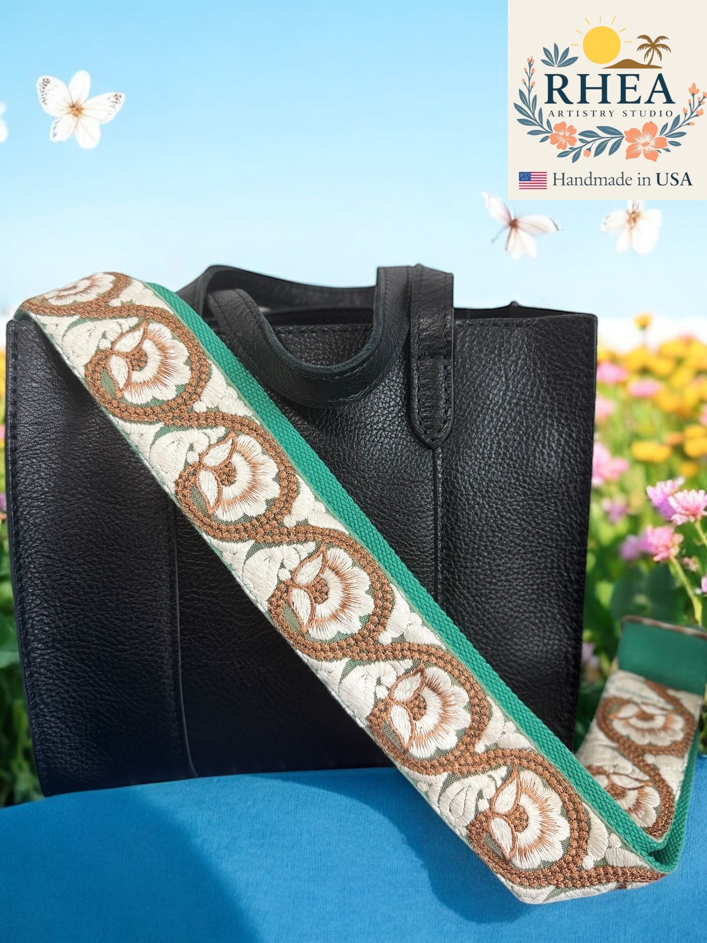 Black handbag with a decorative purse strap featuring floral patterns, set against a natural background with flowers.