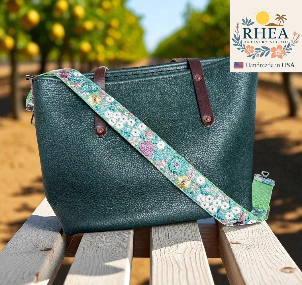Teal handbag with a floral strap on a wooden bench, with RHEA branding in the corner.