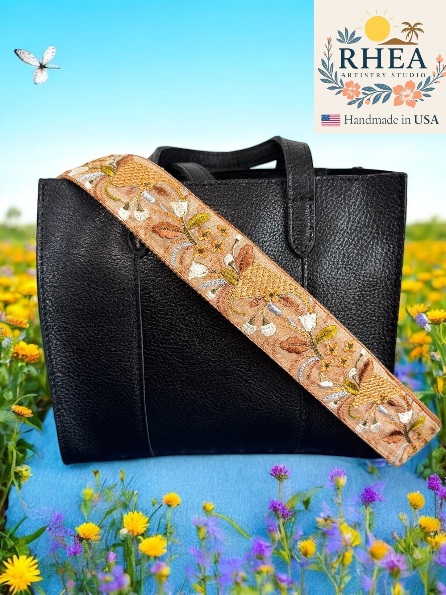 Black handbag with an embroidered purse strap in a field of flowers, featuring the Rhea Artistry Studio logo.