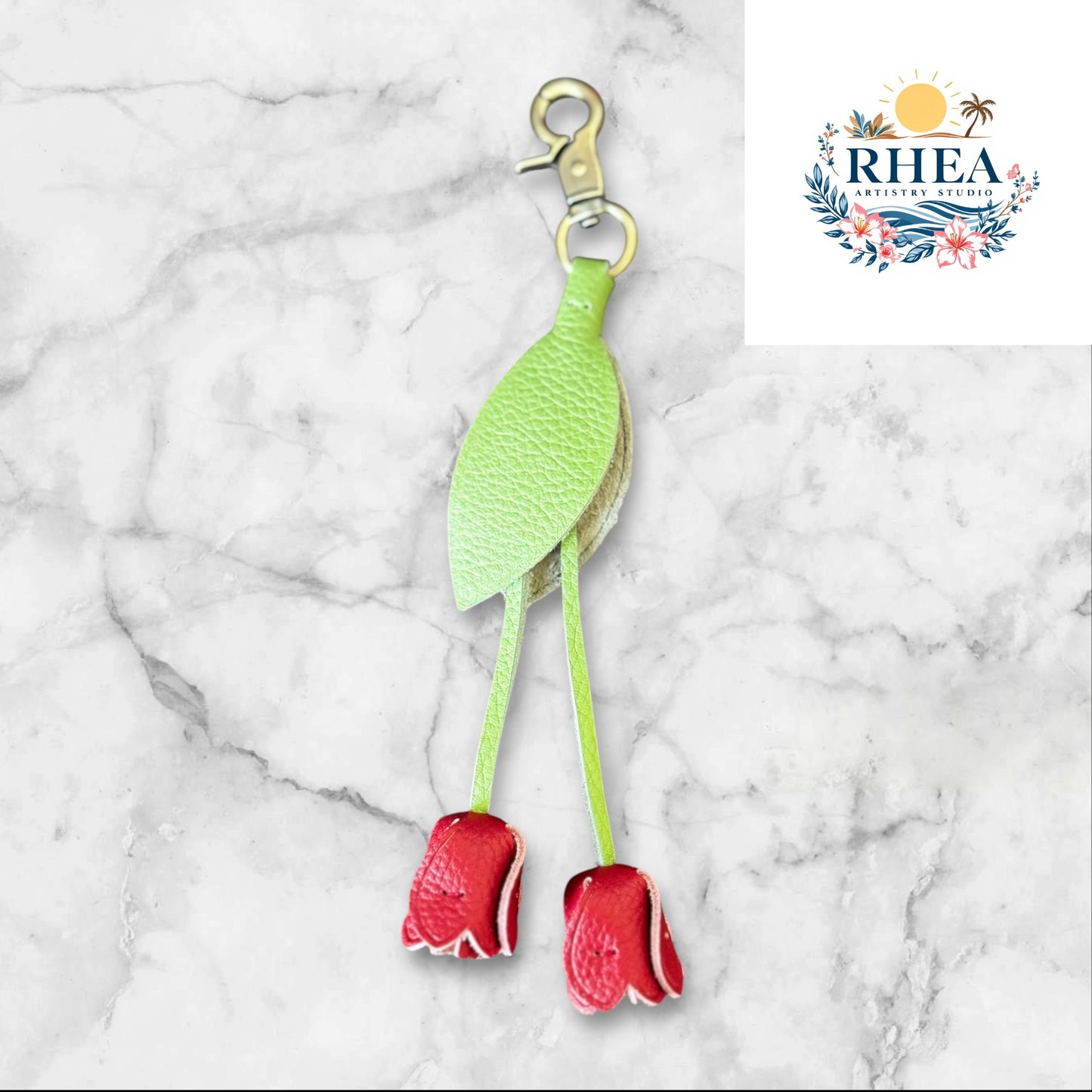 Green and red keychain on a white surface with grass and flowers in the background