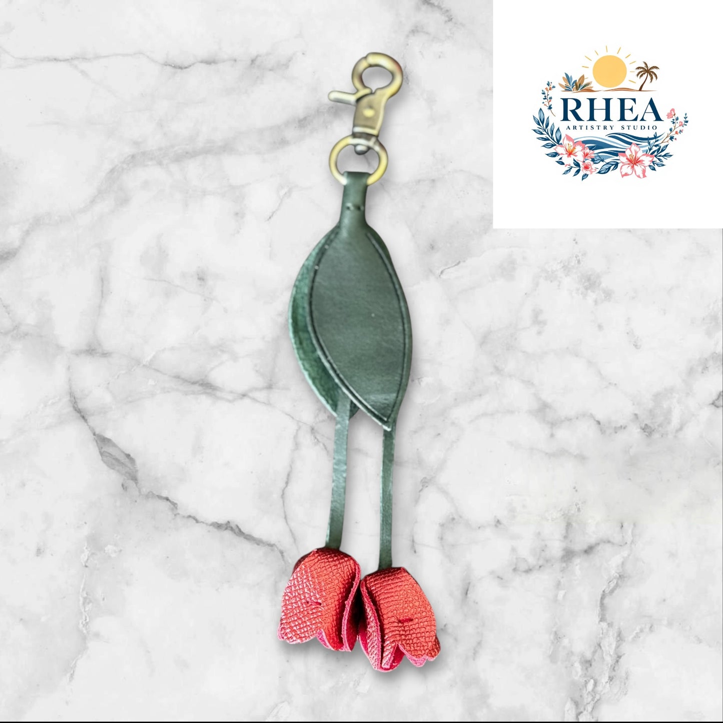 Green and red keychain on a white surface with grass and flowers in the background