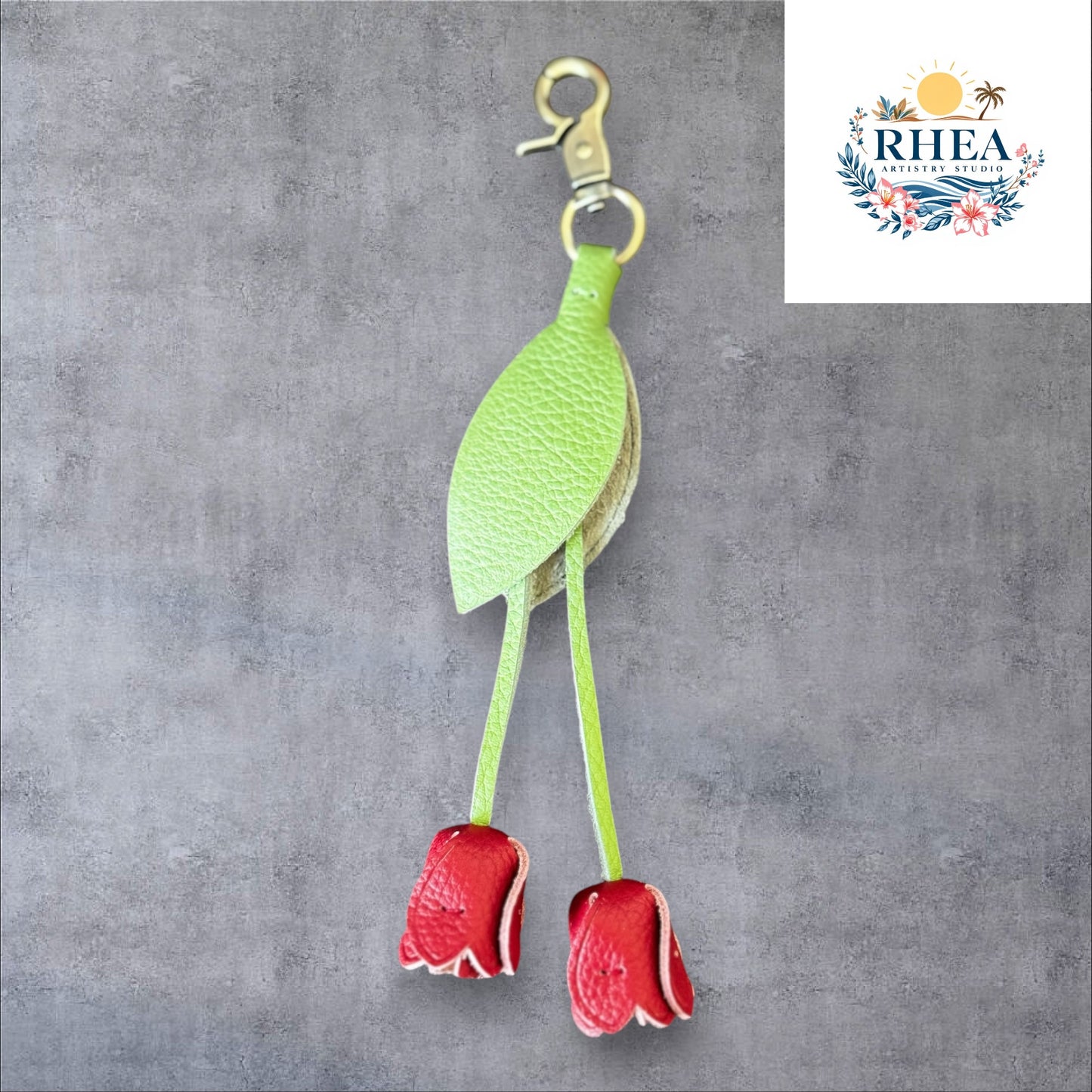 A handmade leather tulip charm with a green leaf and brown floral pattern, attached to a gold lobster clasp on a white marble surface.