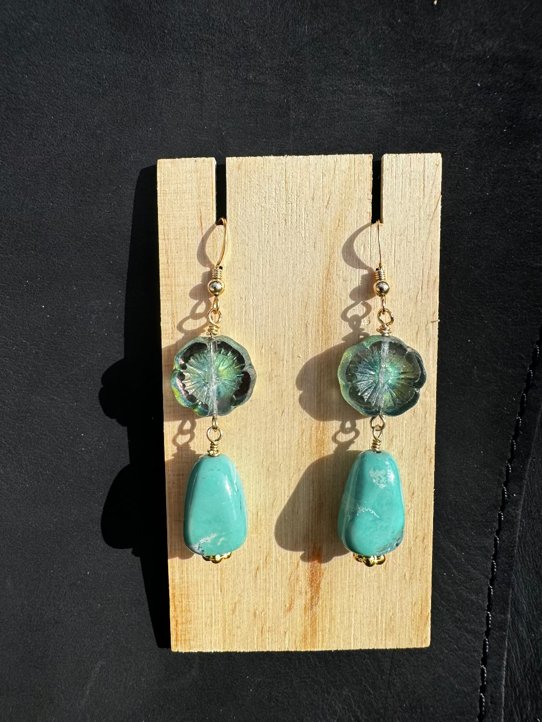 A pair of gold-filled turquoise and hibiscus drop earrings placed on a black surface.