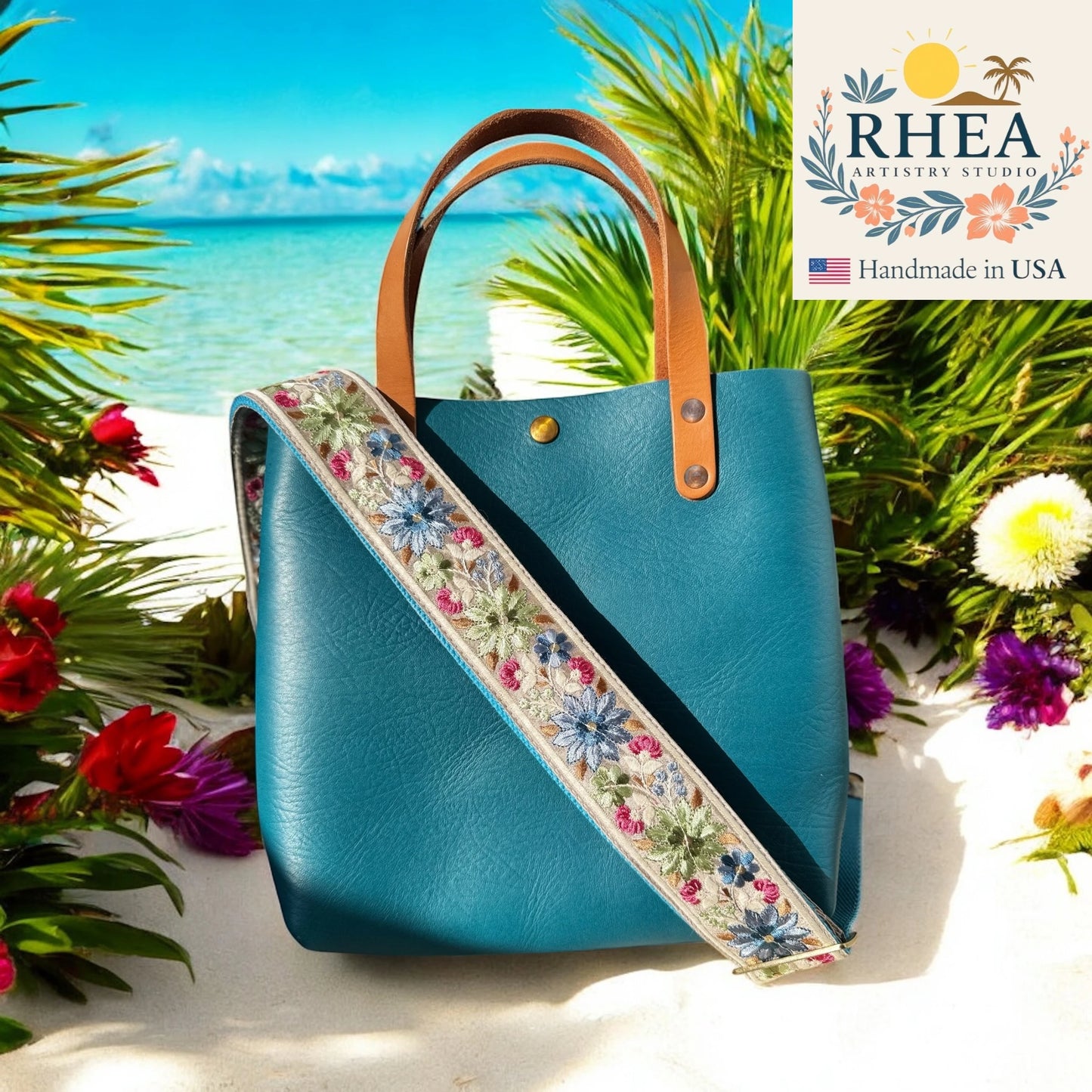 Blue handbag with floral purse strap on a beach background, featuring the RHEA Artistry Studios logo.