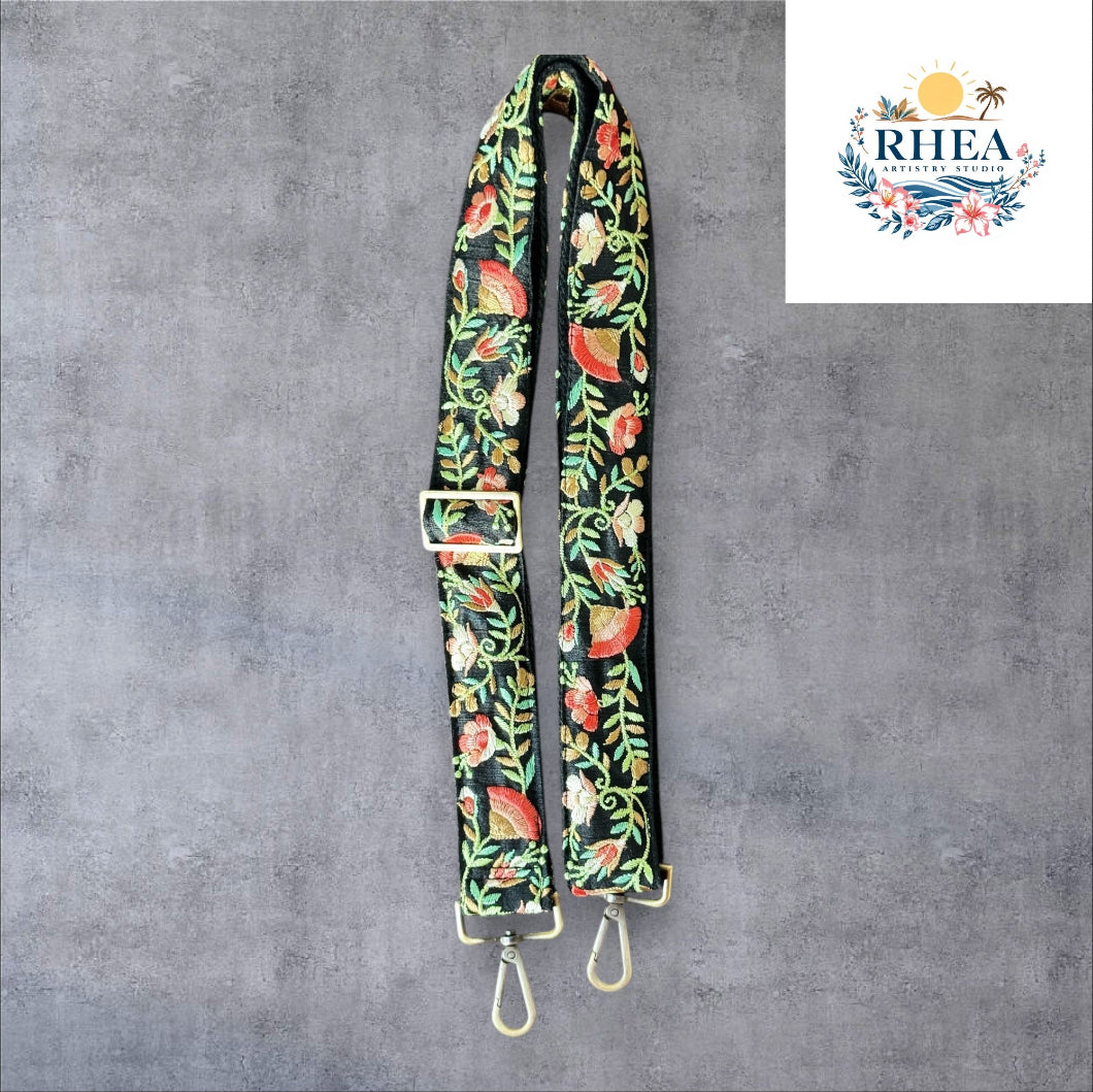 An adjustable embroidered purse strap with a floral pattern and gold hardware, displayed against a grey background.