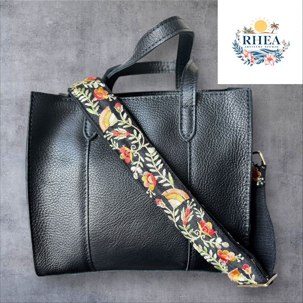 An adjustable embroidered purse strap with a floral pattern and gold hardware, displayed against a grey background.