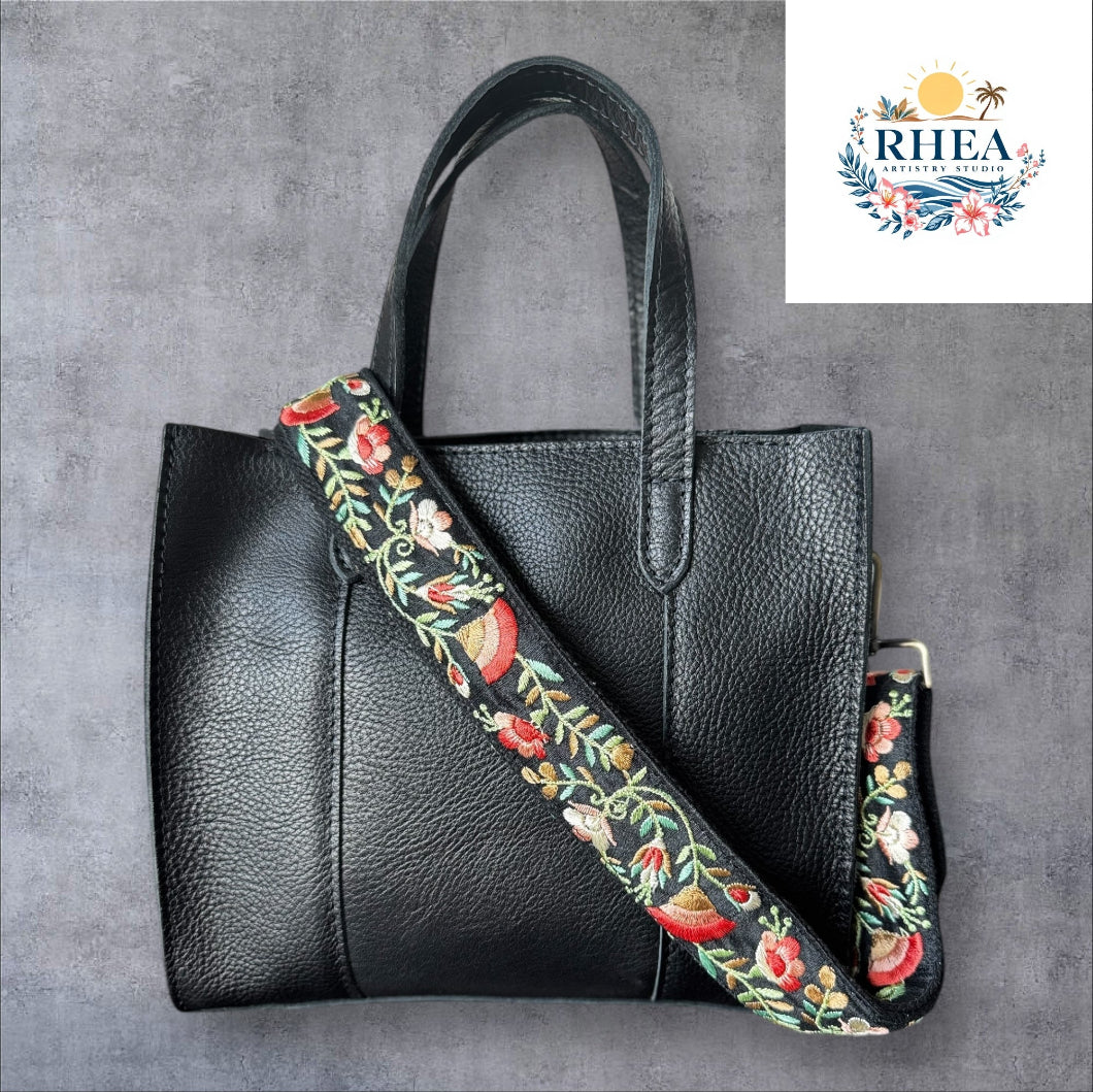An adjustable embroidered purse strap with a floral pattern and gold hardware, displayed against a grey background.
