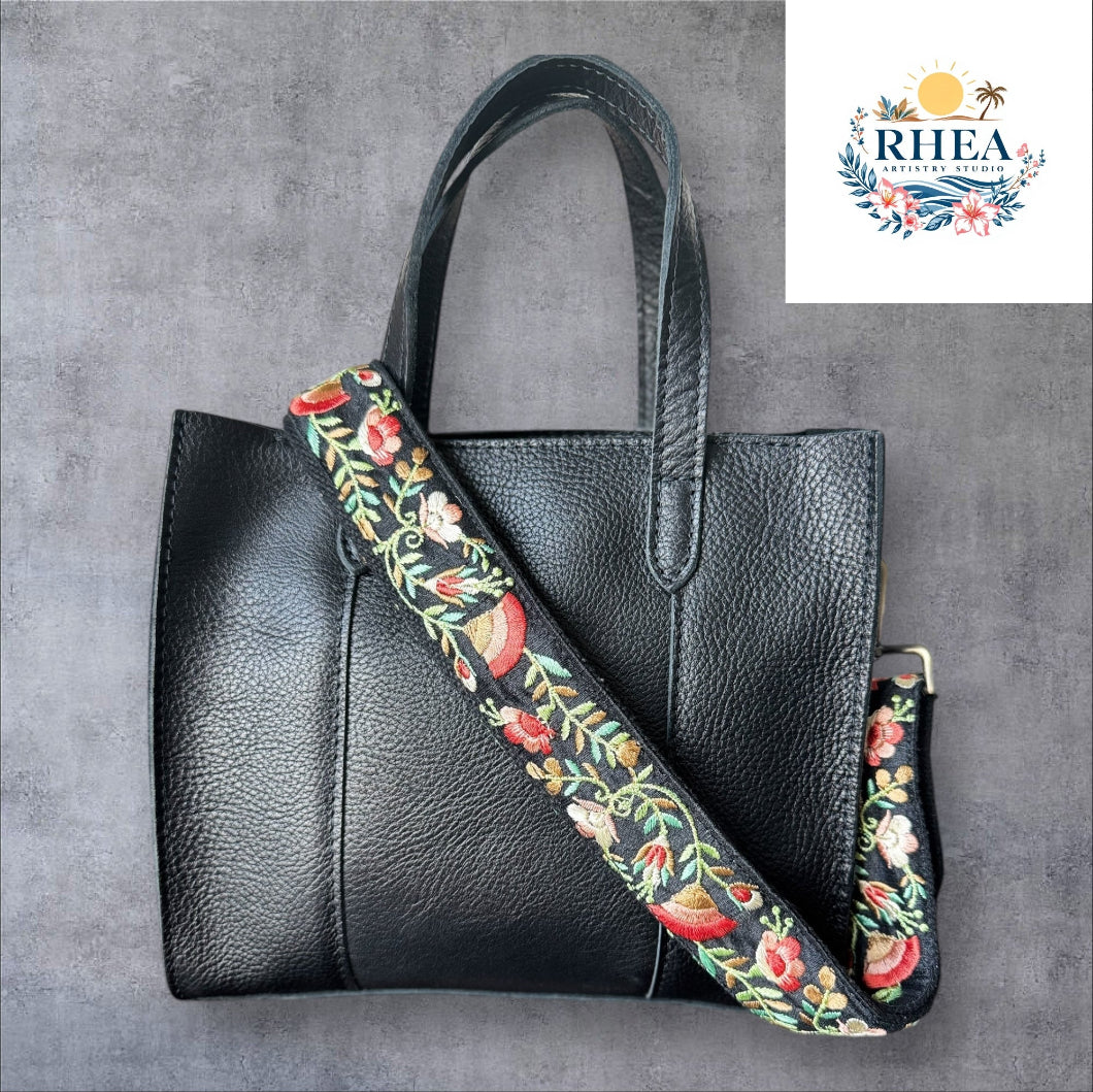 An adjustable embroidered purse strap with a floral pattern and gold hardware, displayed against a grey background.