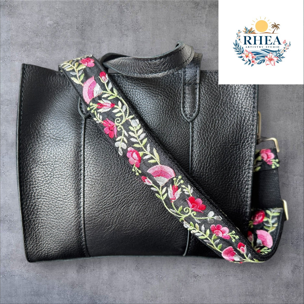 An adjustable embroidered purse strap with a floral pattern and gold hardware, displayed against a grey background.