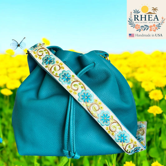 Blue bag with a floral purse strap against a background of yellow flowers and a blue sky.