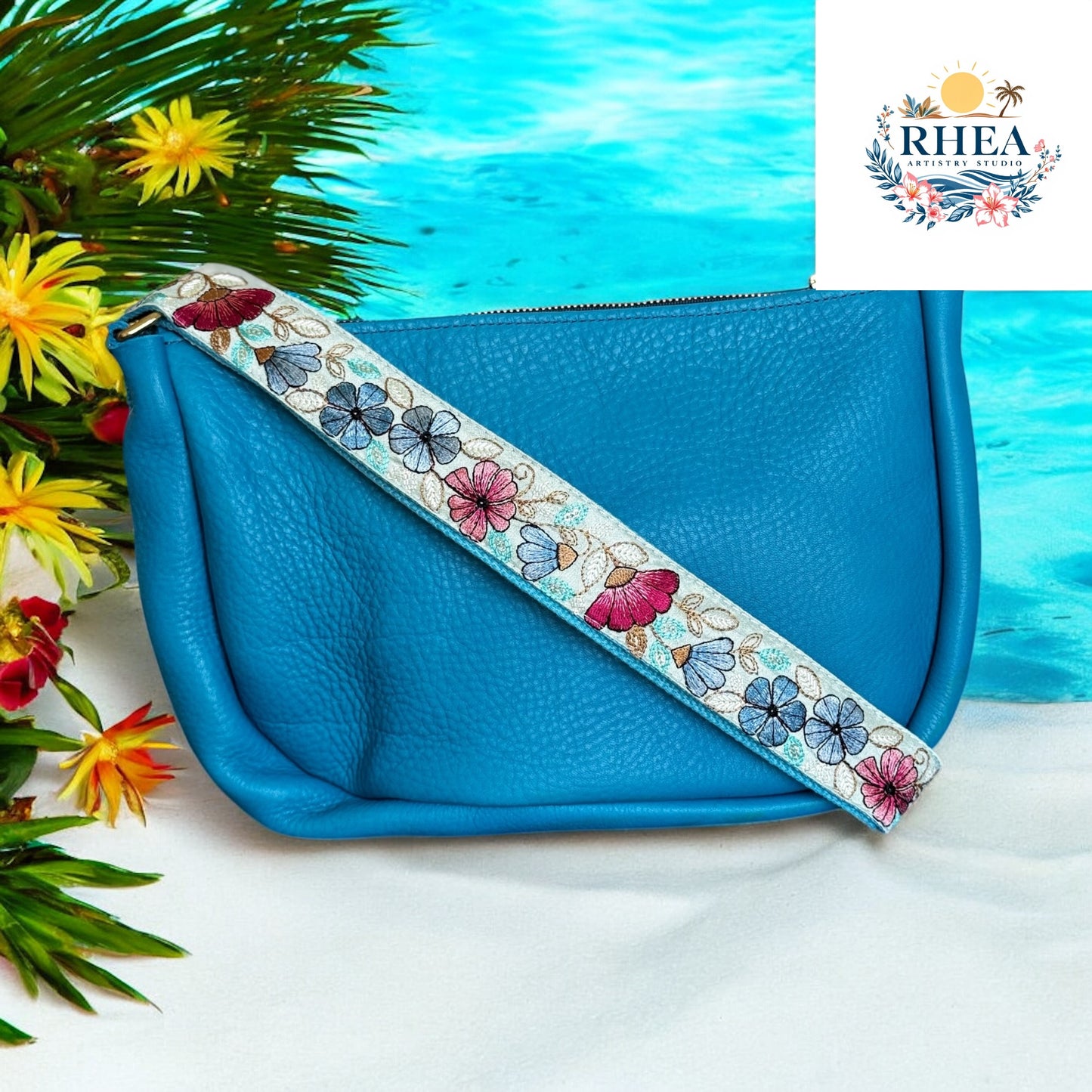Aqua leather bag with light blue strap featuring floral embroidery in aqua, lime, and gold at beach