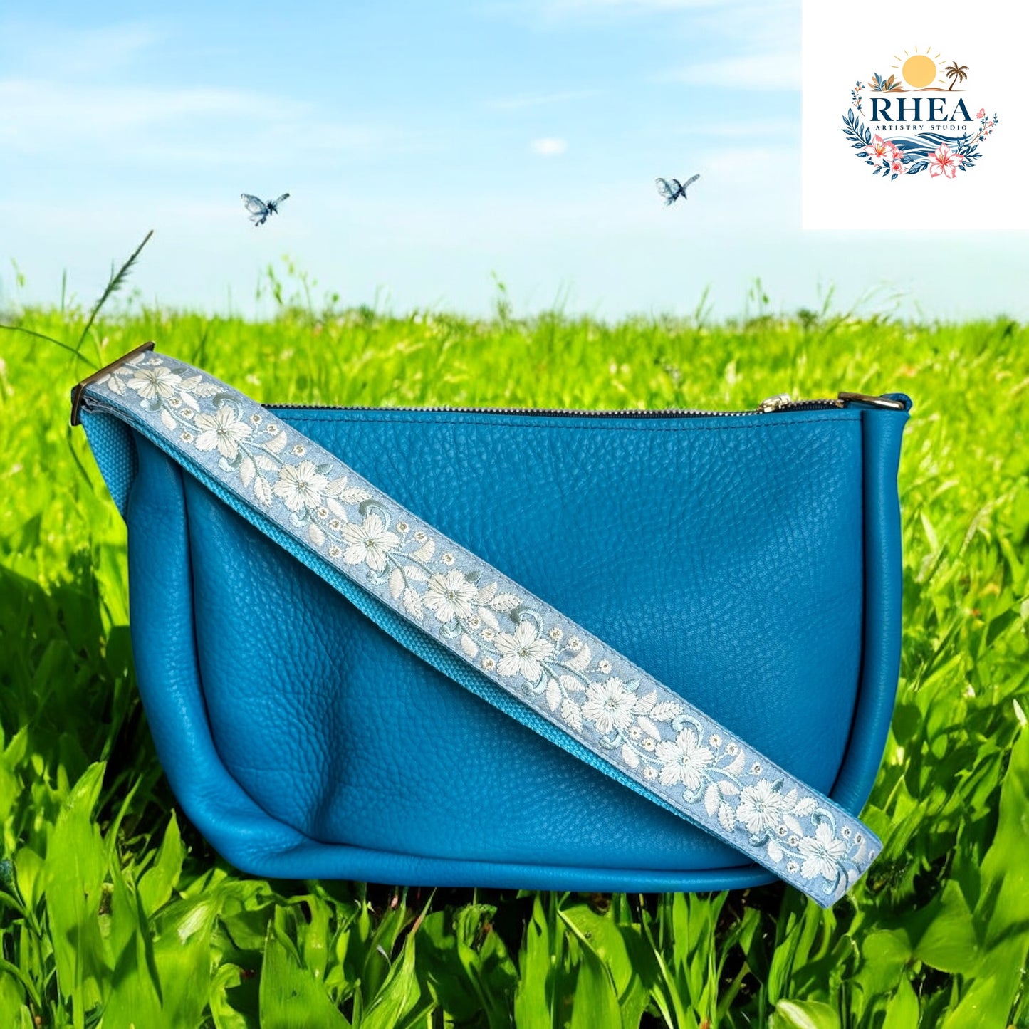 Blue handbag with floral strap on grass with 'RHEA' logo