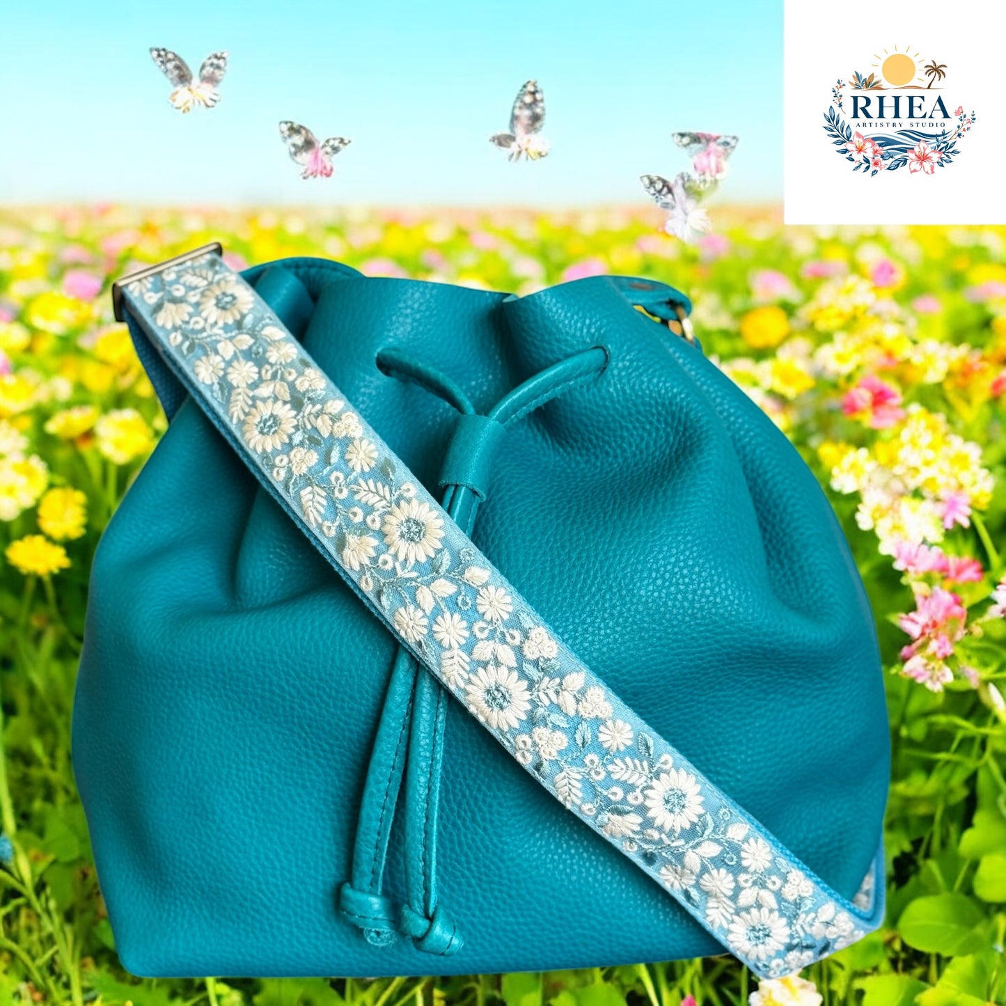 Handcrafted aqua floral handbag strap with ivory embroidery, 1.5-inch wide crossbody style with a soft fabric base. Ideal for summer bags and coastal-inspired fashion against a meadow background
