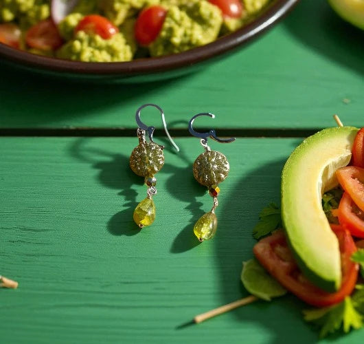 Gold earrings with yellow teardrop stones on a green surface with food items.
