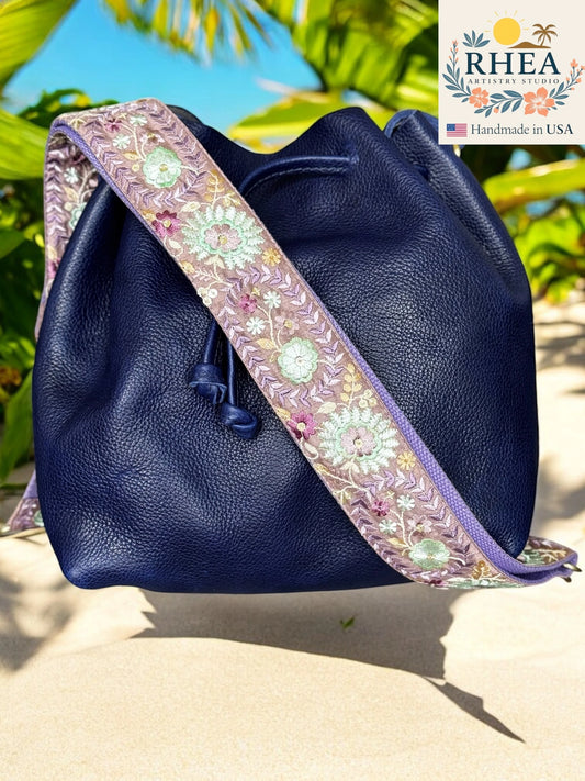 Navy blue leather bag with a floral purse strap on a sandy background