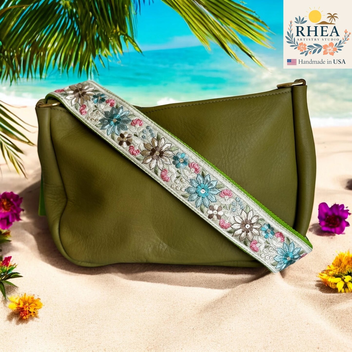 Green handbag with floral purse strap on a beach setting, featuring the RHEA brand.