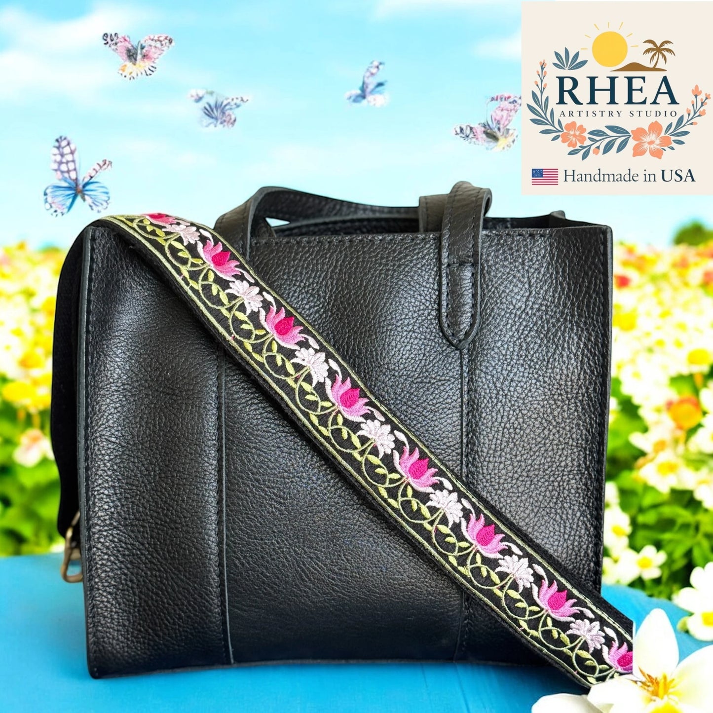 Black leather handbag with floral purse strap against a colorful background, featuring the RHEA Artistry Studios logo.