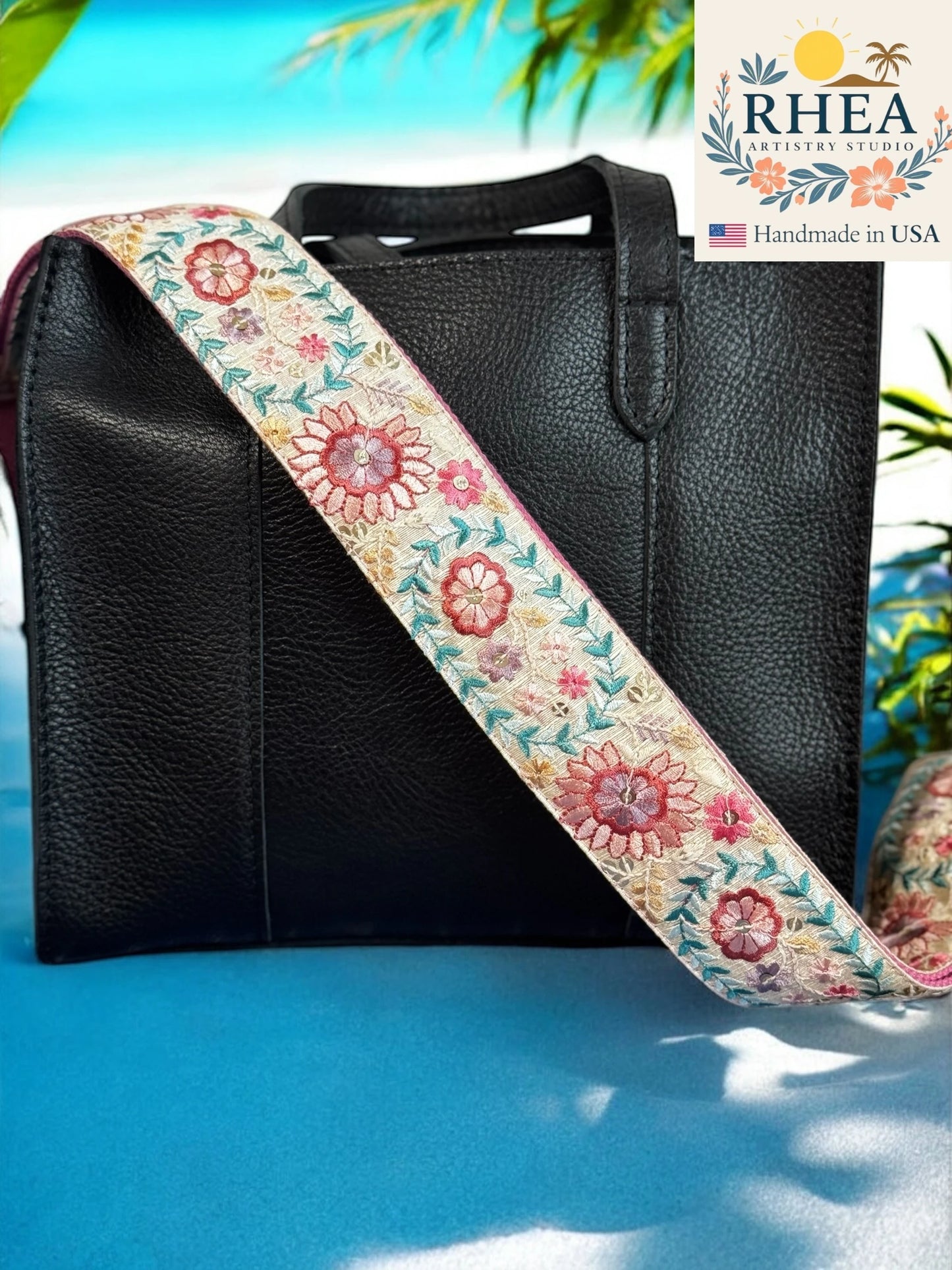 Black leather bag with a floral purse strap on a blue surface, RHEA brand visible.