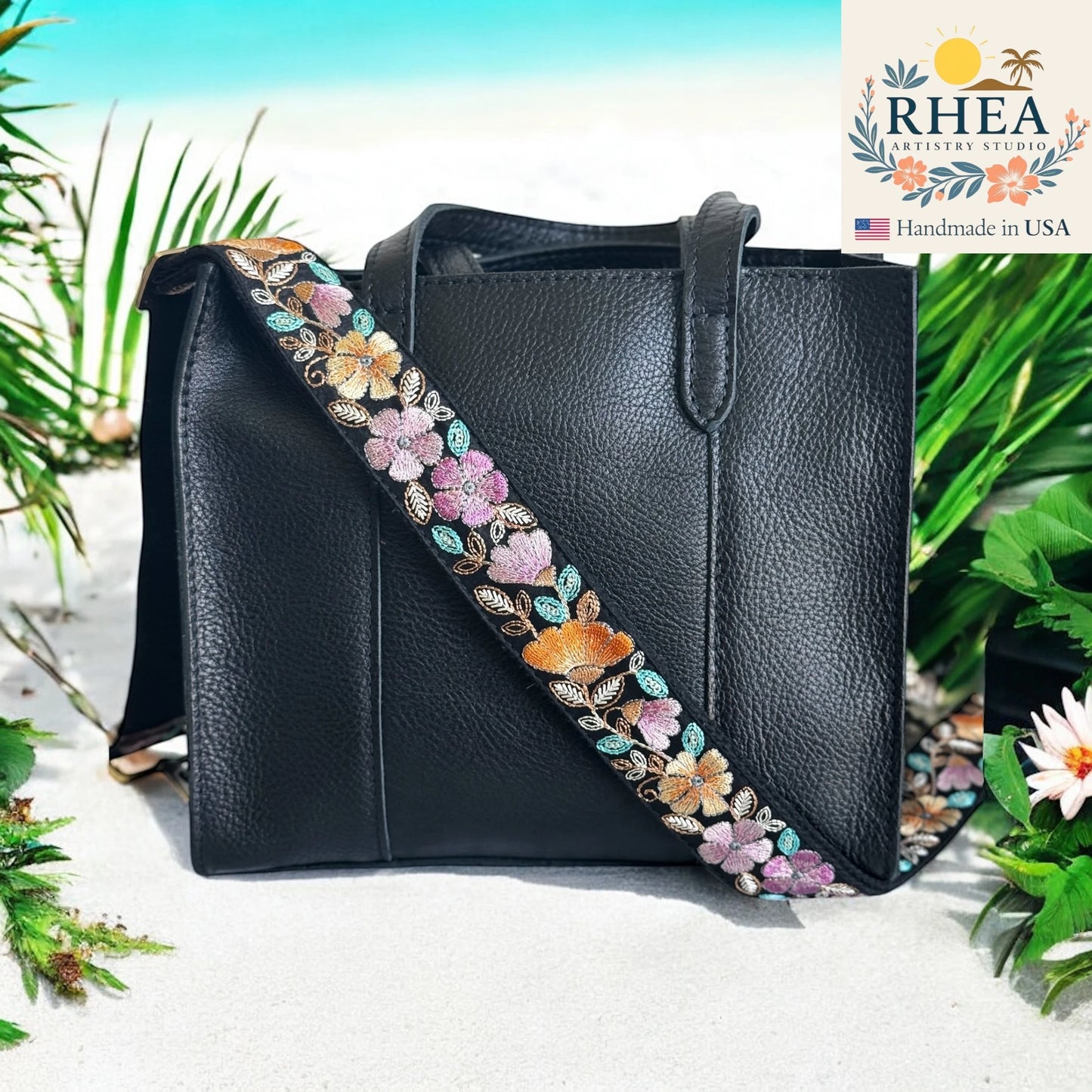 Black handbag with a floral purse strap on a beach background, featuring the RHEA brand.