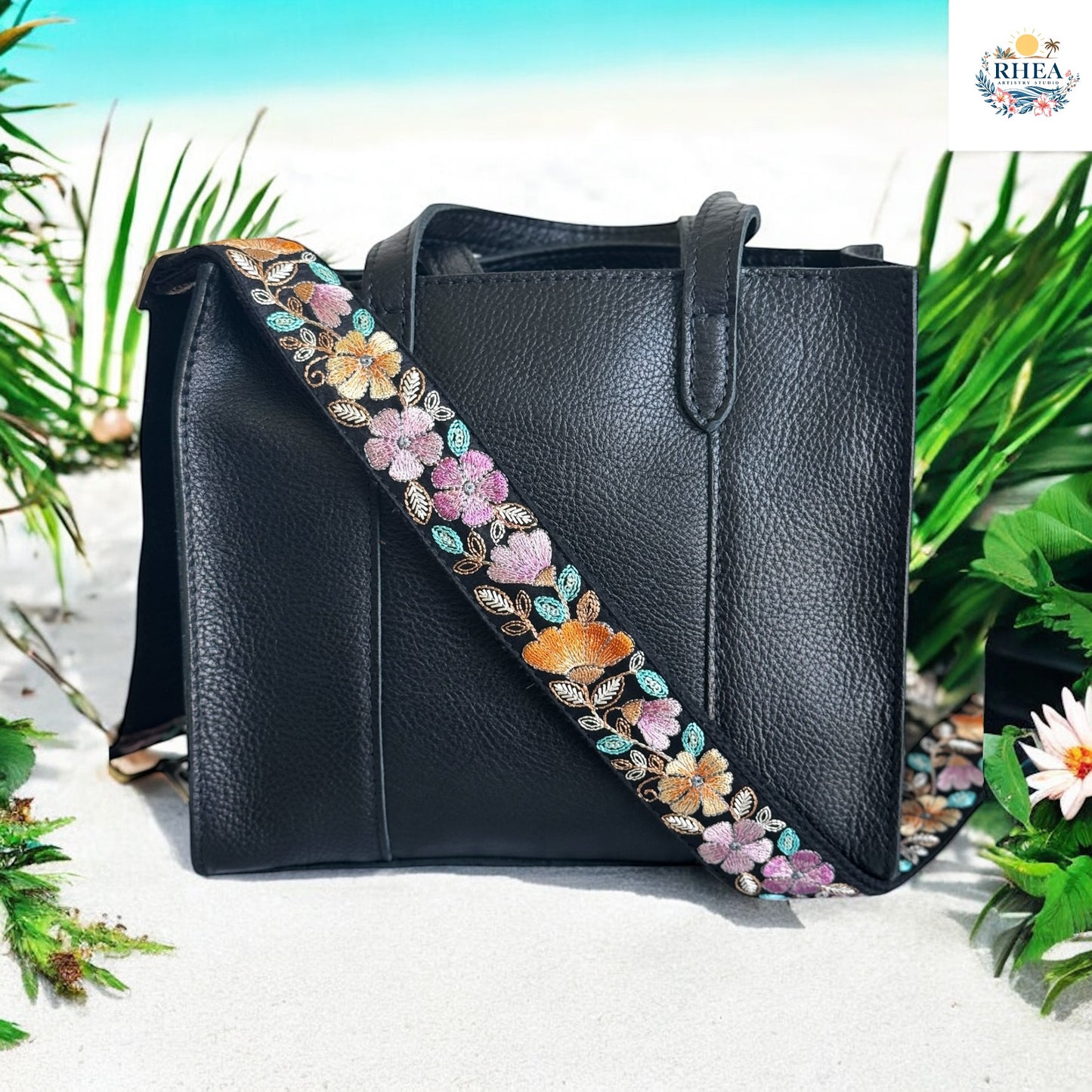 Black leather tote with a pastel floral embroidered strap in blush, lavender, and amber.