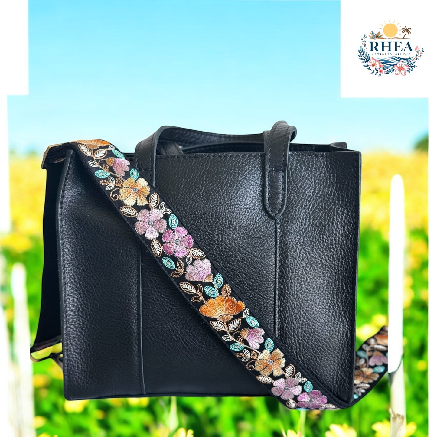 Black leather tote with a pastel floral embroidered strap in blush, lavender, and amber.