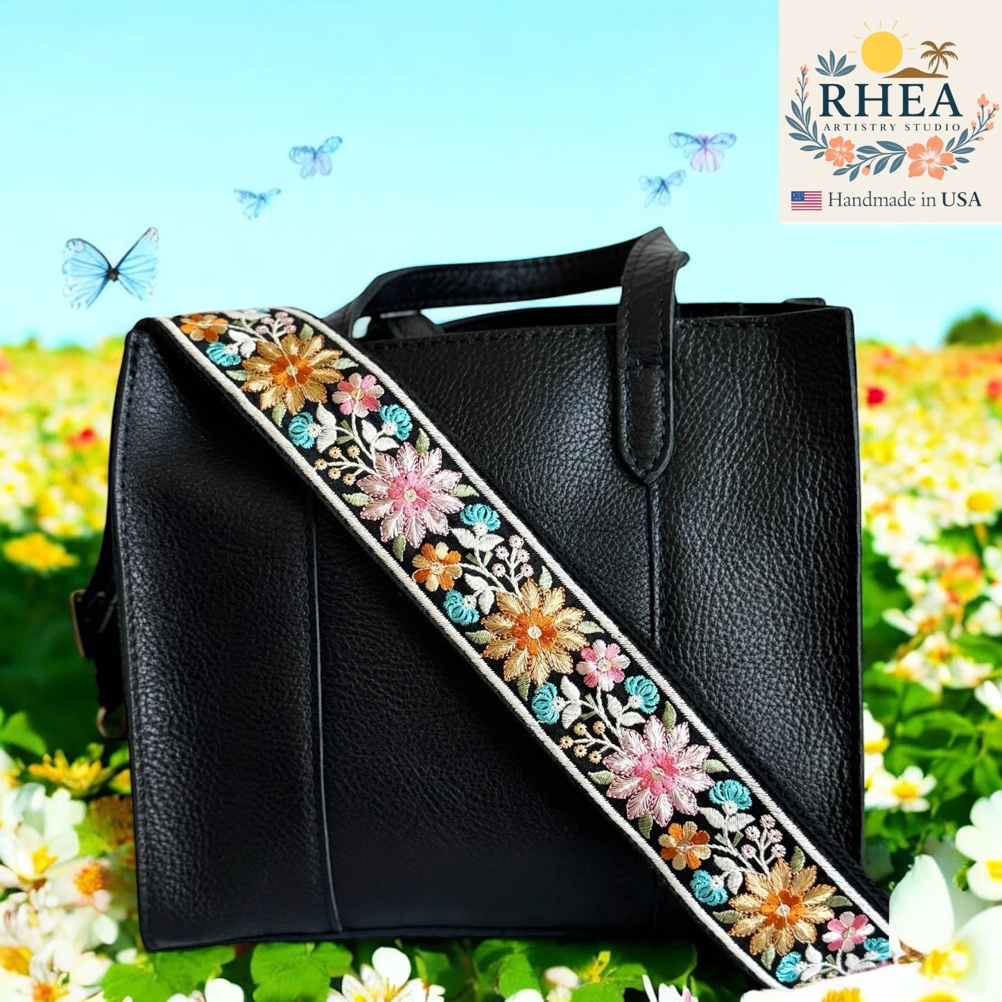 Black handbag with floral embroidery purse strap against a floral background, featuring the RHEA Artisans Studio logo.