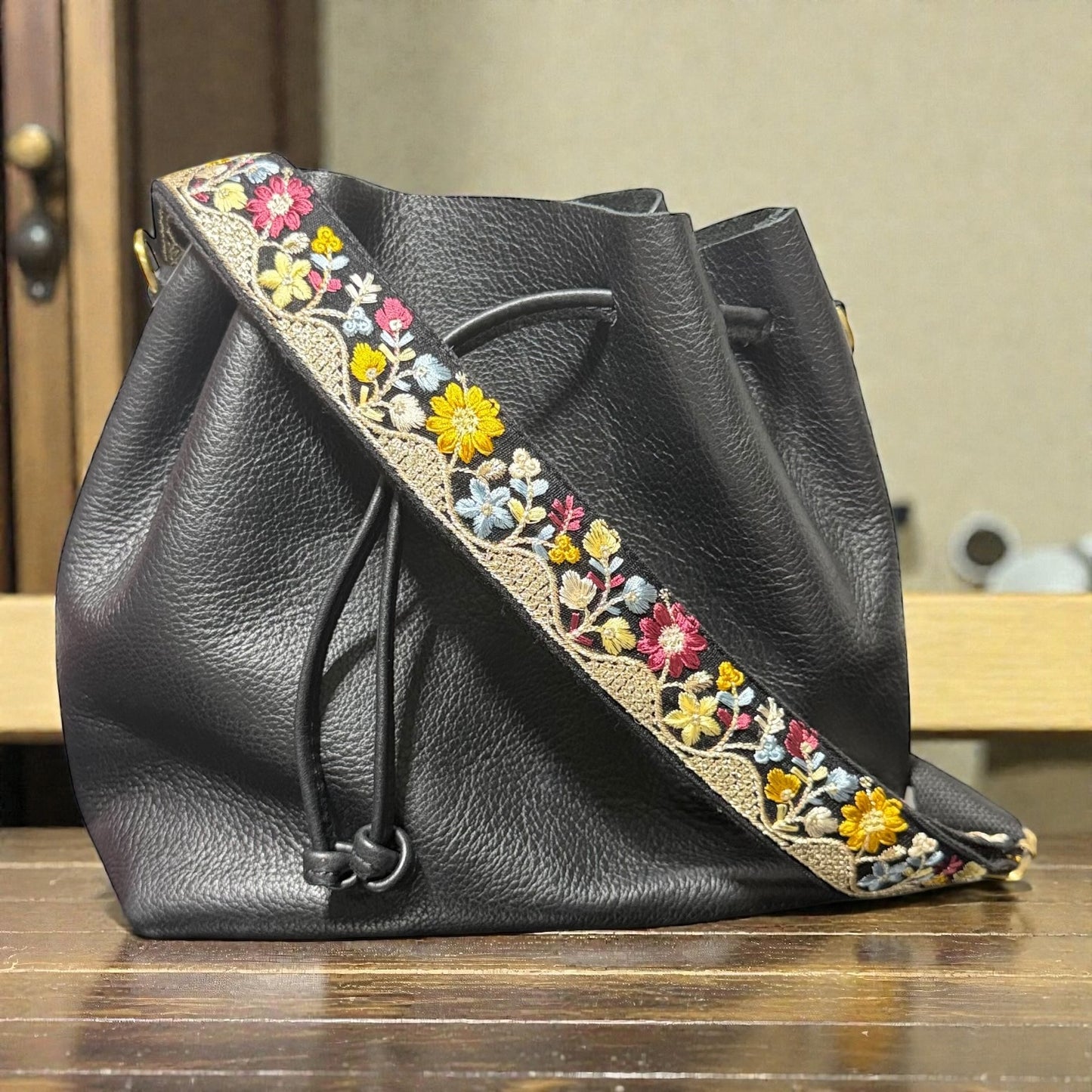 Black leather bag with colorful floral embroidery on a wooden surface