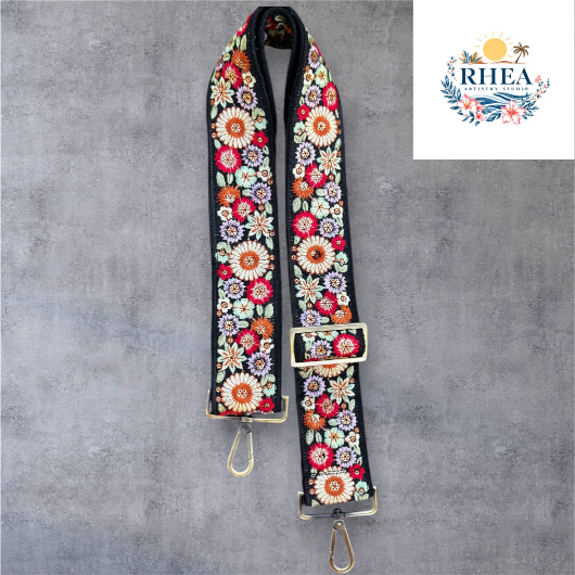 A floral embroidered purse strap in multicolor, attached to a black leather bag with brushed brass hardware.