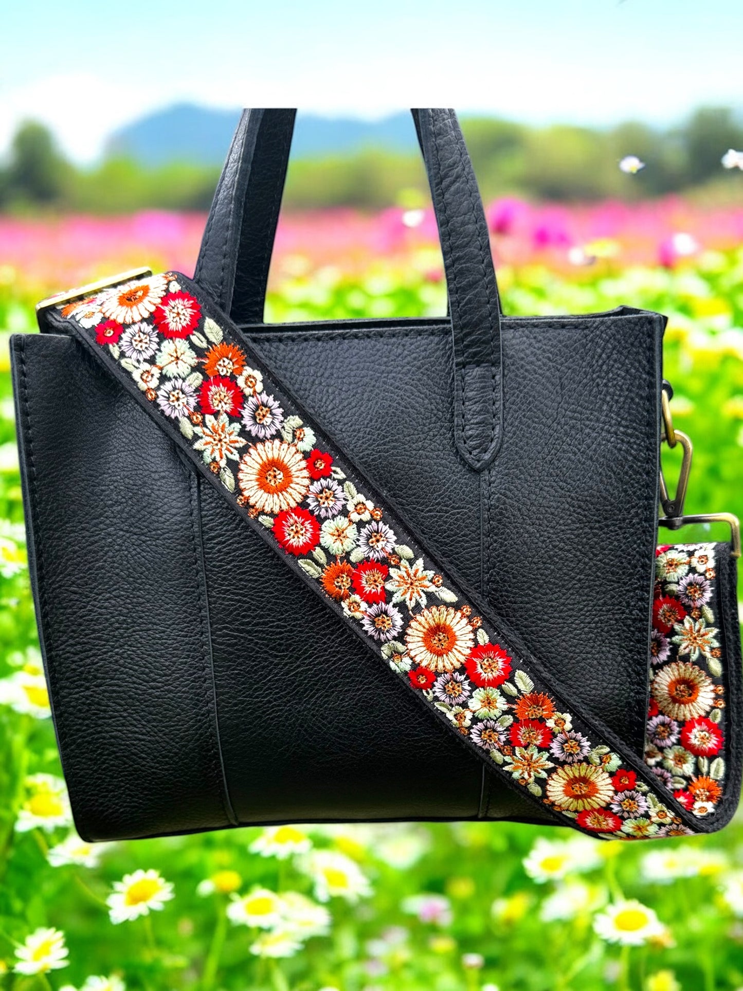 A floral embroidered purse strap in multicolor, attached to a black leather bag with brushed brass hardware.