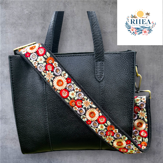 A floral embroidered purse strap in multicolor, attached to a black leather bag with brushed brass hardware.