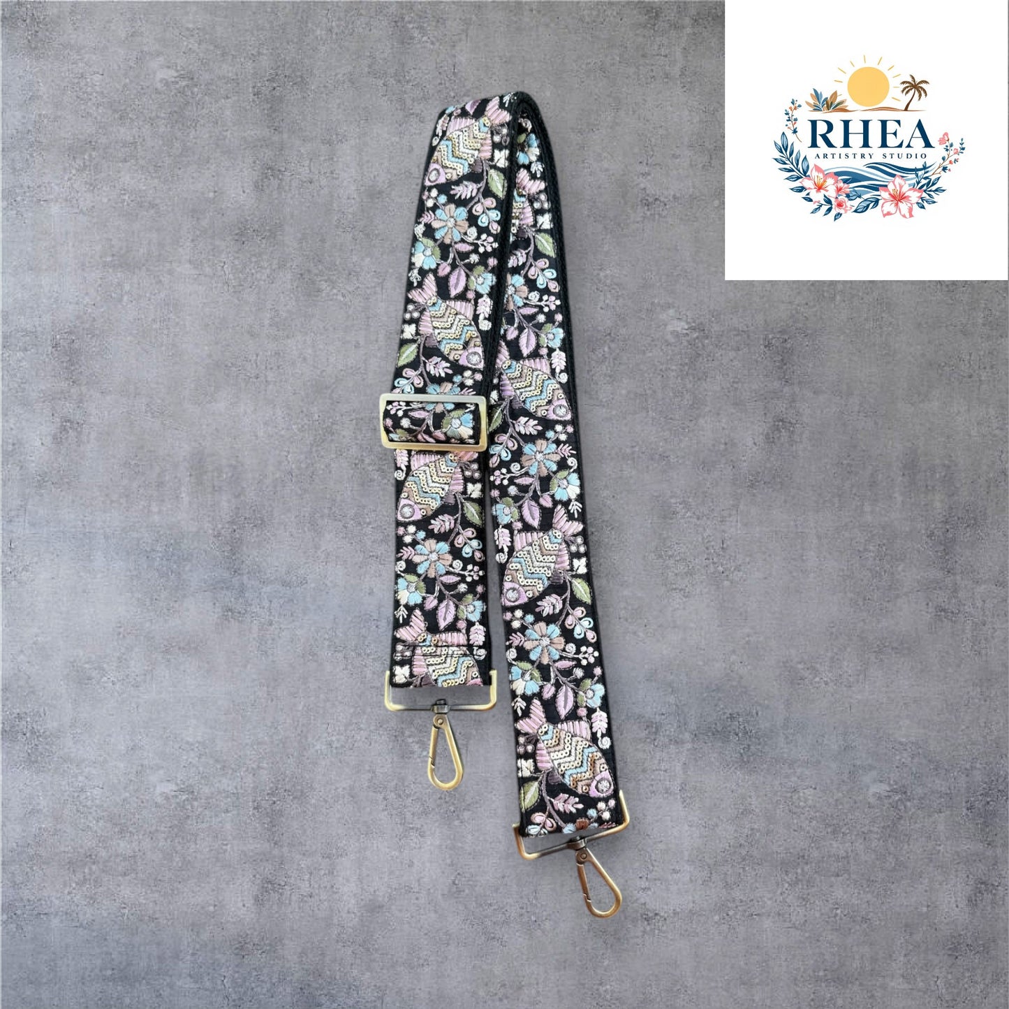 Adjustable embroidered purse strap with floral patterns and gold hardware, displayed on a gray background.