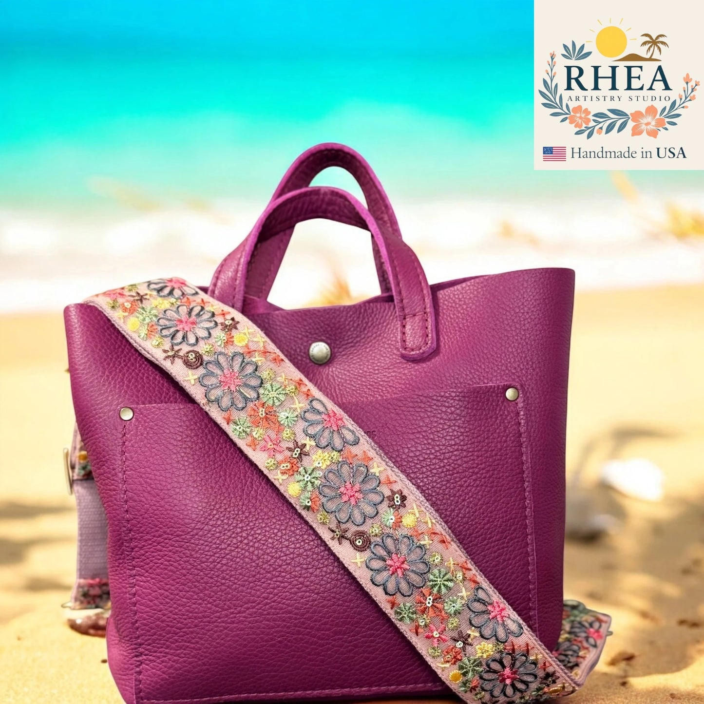 Purple handbag with a floral strap on a beach, featuring the RHEA brand.