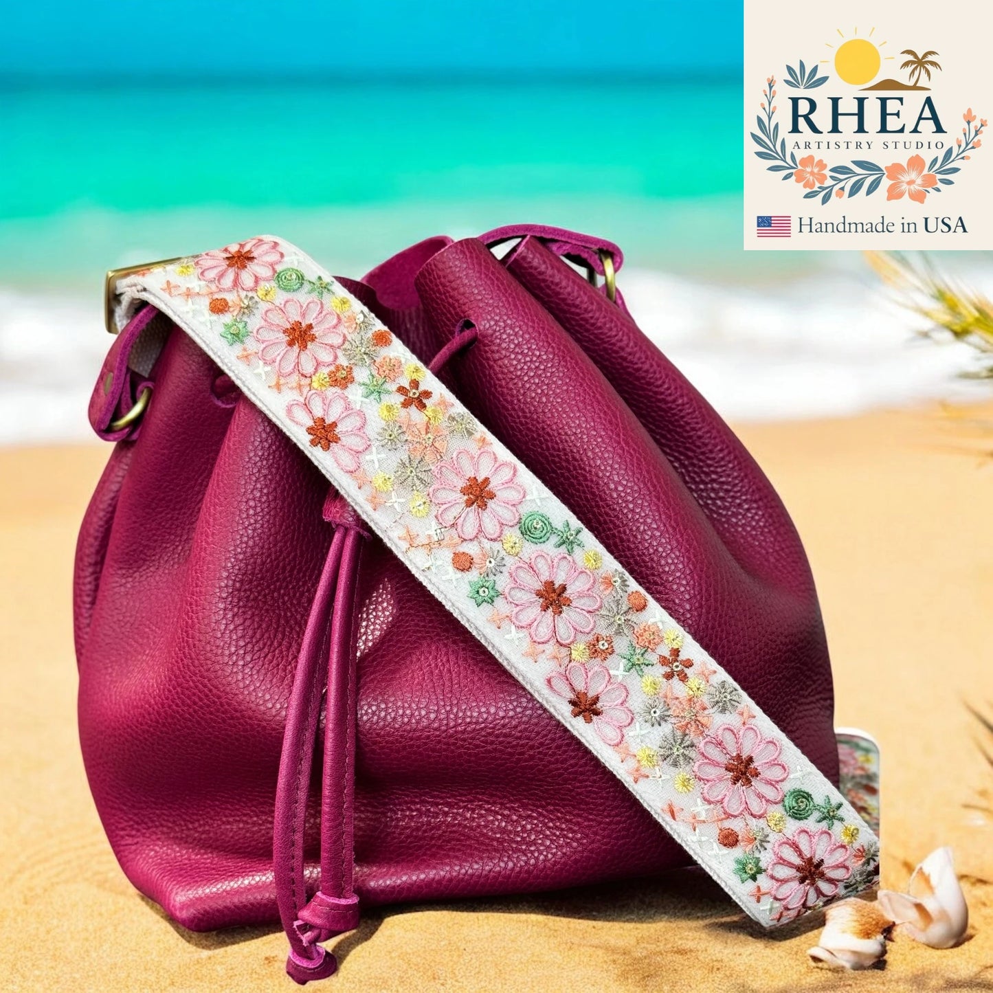 Pink drawstring bag with a floral strap on a beach, featuring the RHEA brand.