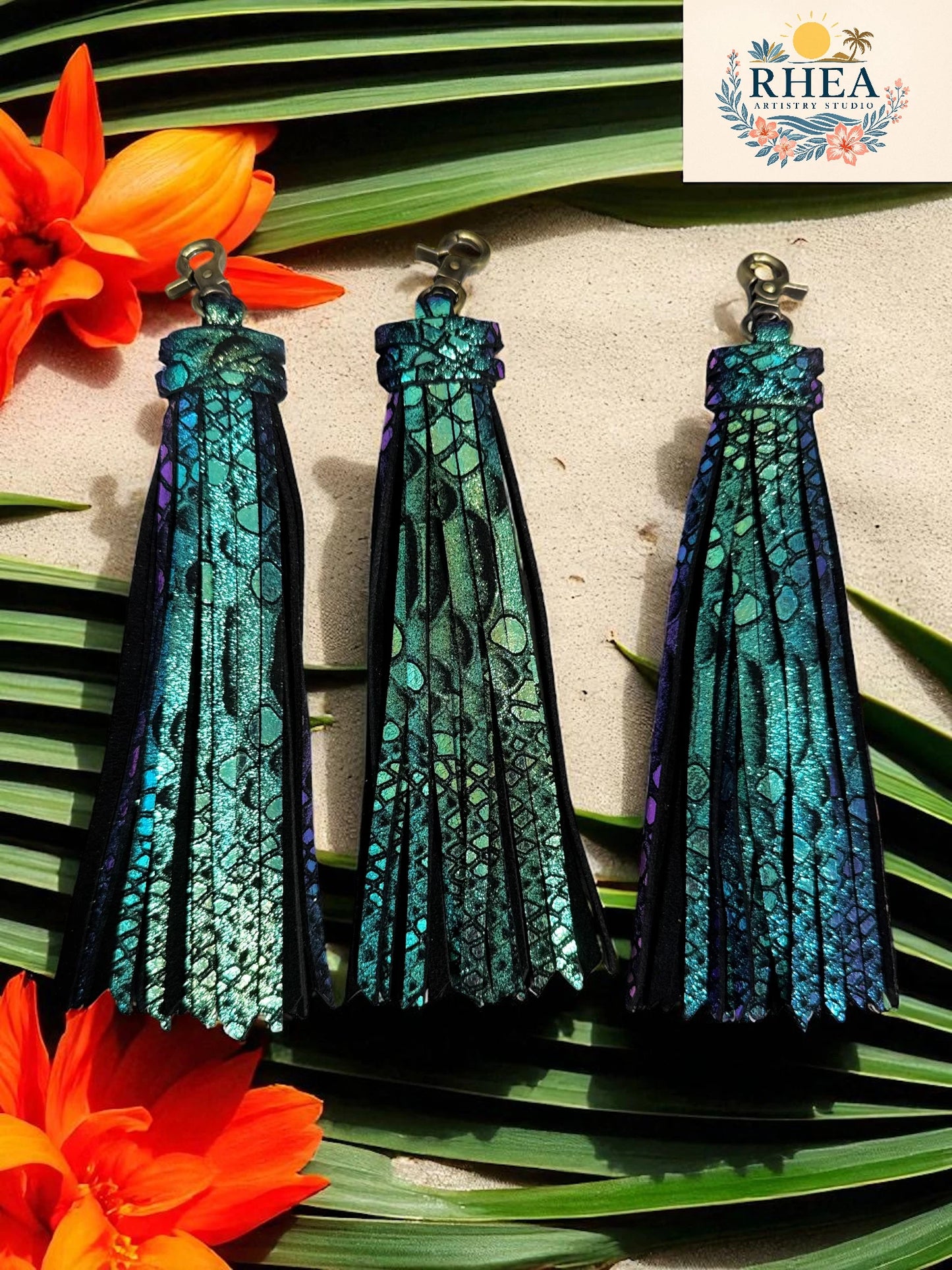Blue and green patterned earrings on a leaf with RHEA branding.