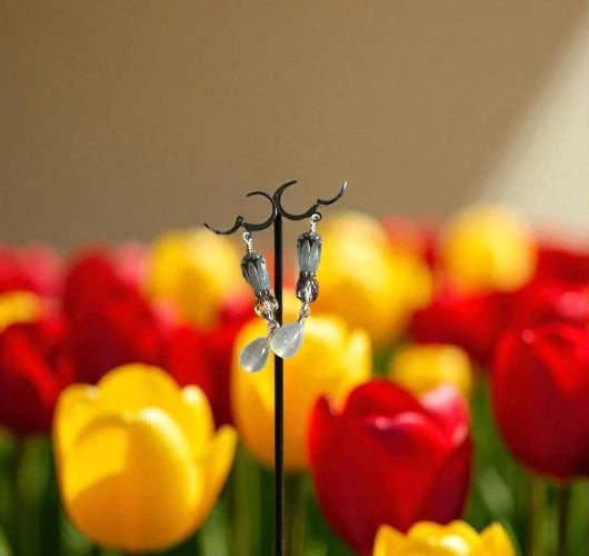 Pair of earrings on a stand with red and yellow tulips in the background