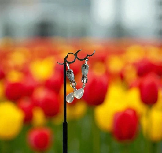 Pair of earrings on a stand with a blurred background of red and yellow flowers