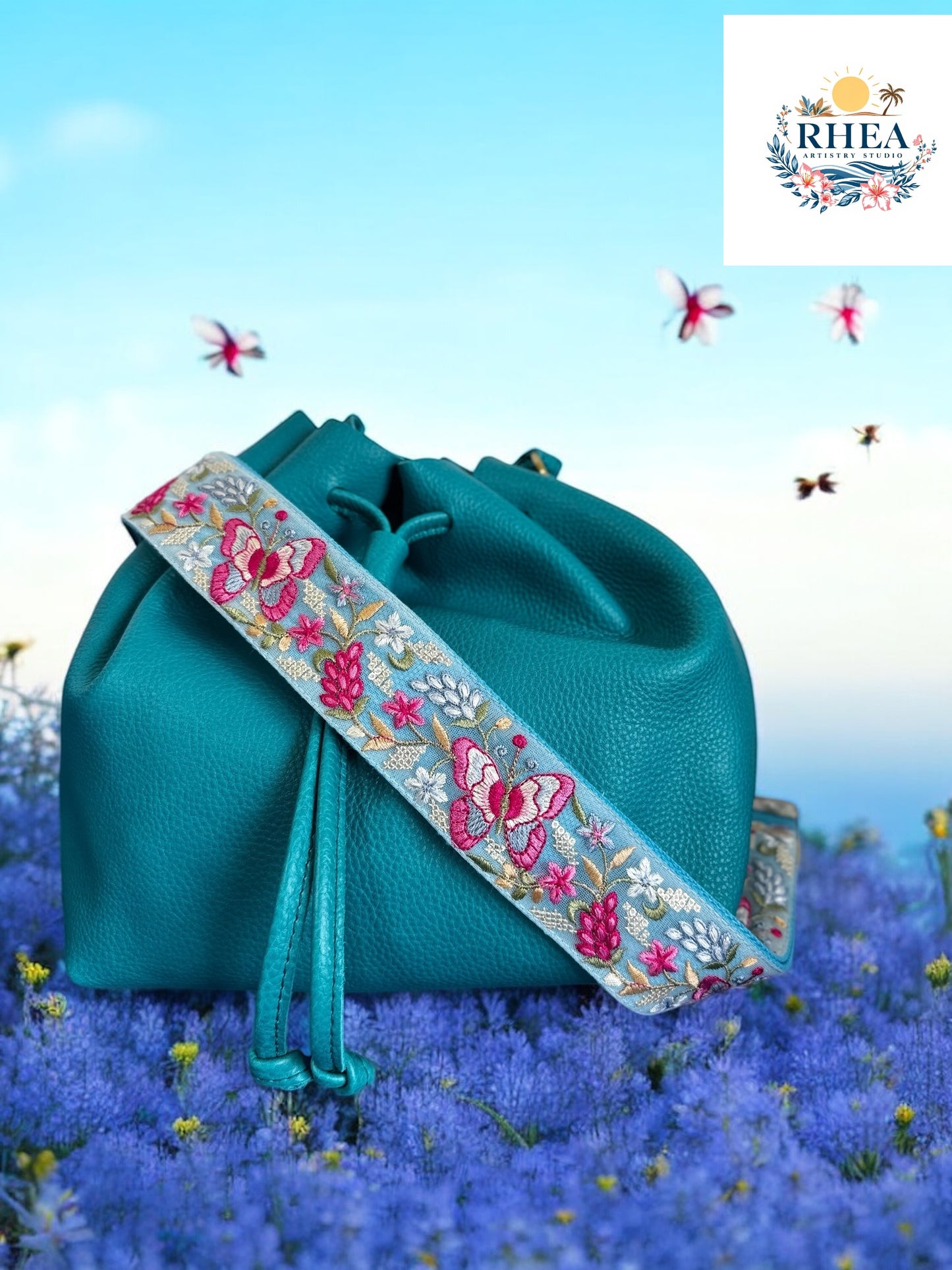 A black purse with a pink and green floral embroidered strap placed on a blue surface with flowers in the background.