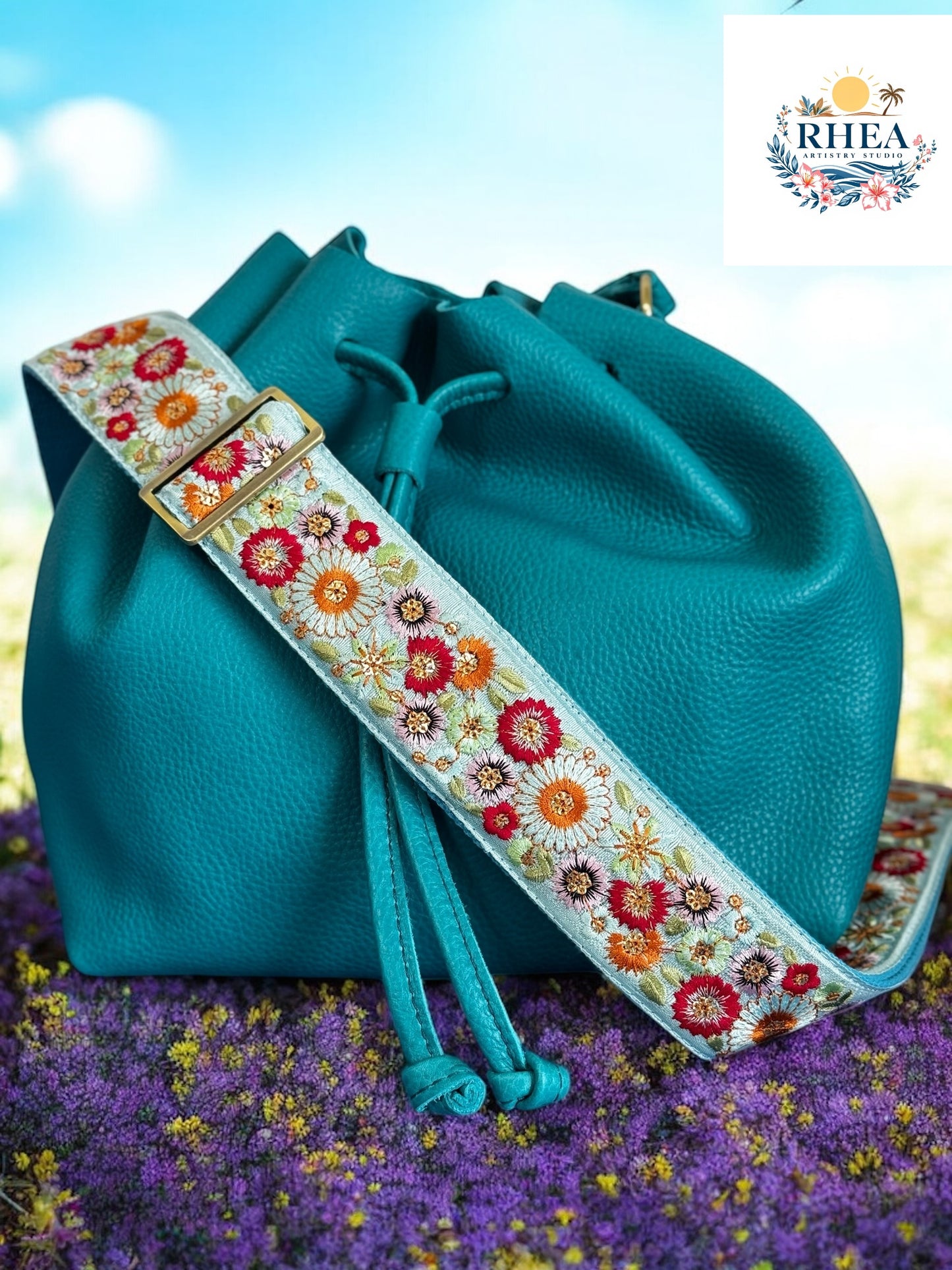 A floral embroidered purse strap in multicolor, attached to a black leather bag with brushed brass hardware.